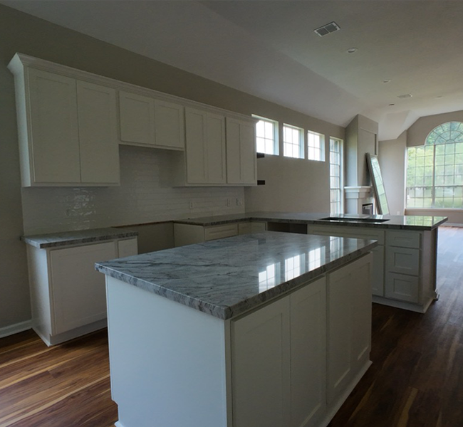 Modern kitchen with white cabinets, gray marble countertops, and hardwood flooring under natural light.