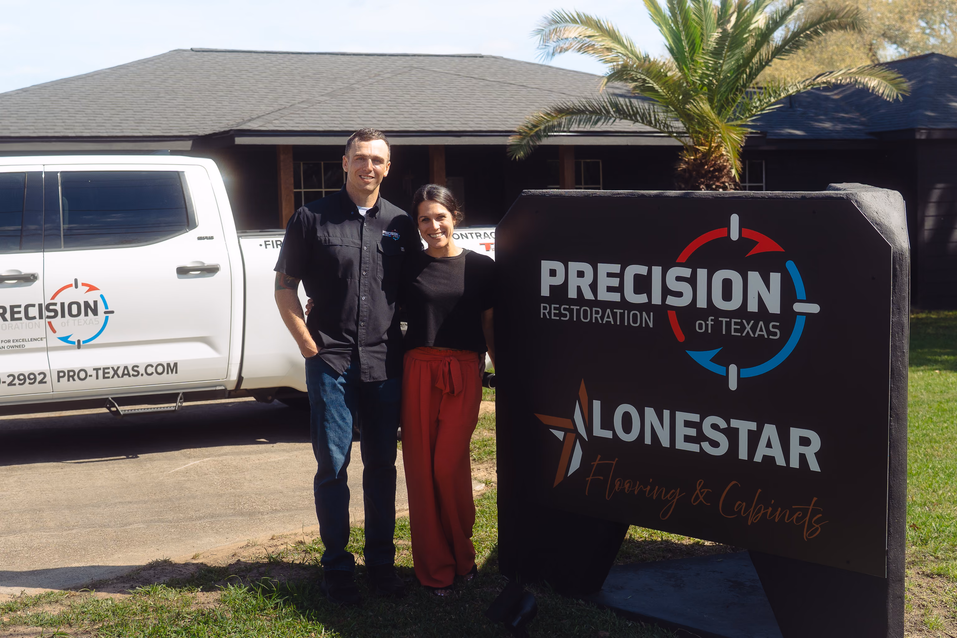A man and woman stand smiling by a Precision Restoration and Lonestar Flooring sign and company truck.