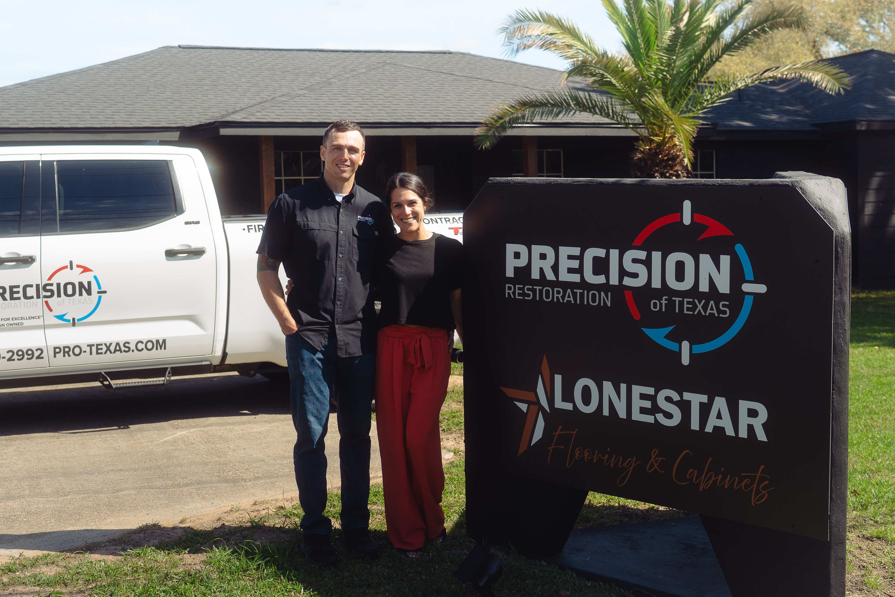 A man and woman stand smiling by a Precision Restoration and Lonestar Flooring sign and company truck.