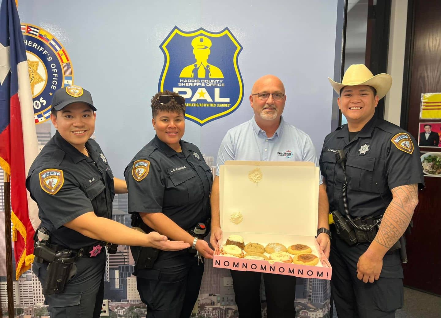 Three sheriff officers and a man holding a box of assorted cookies with 'NOMNOMNOMNOM!' text.
