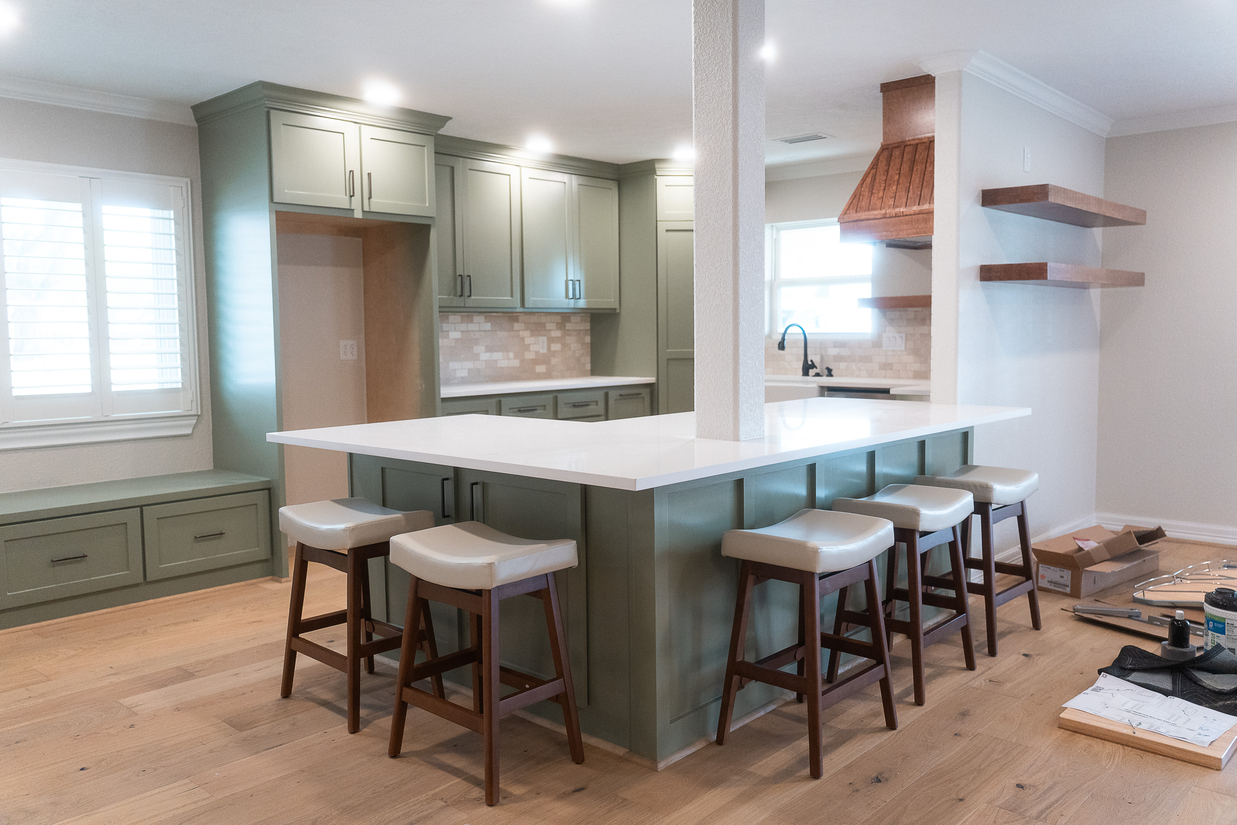 Modern kitchen with green cabinetry, white countertop island, five stools, and wooden floor.