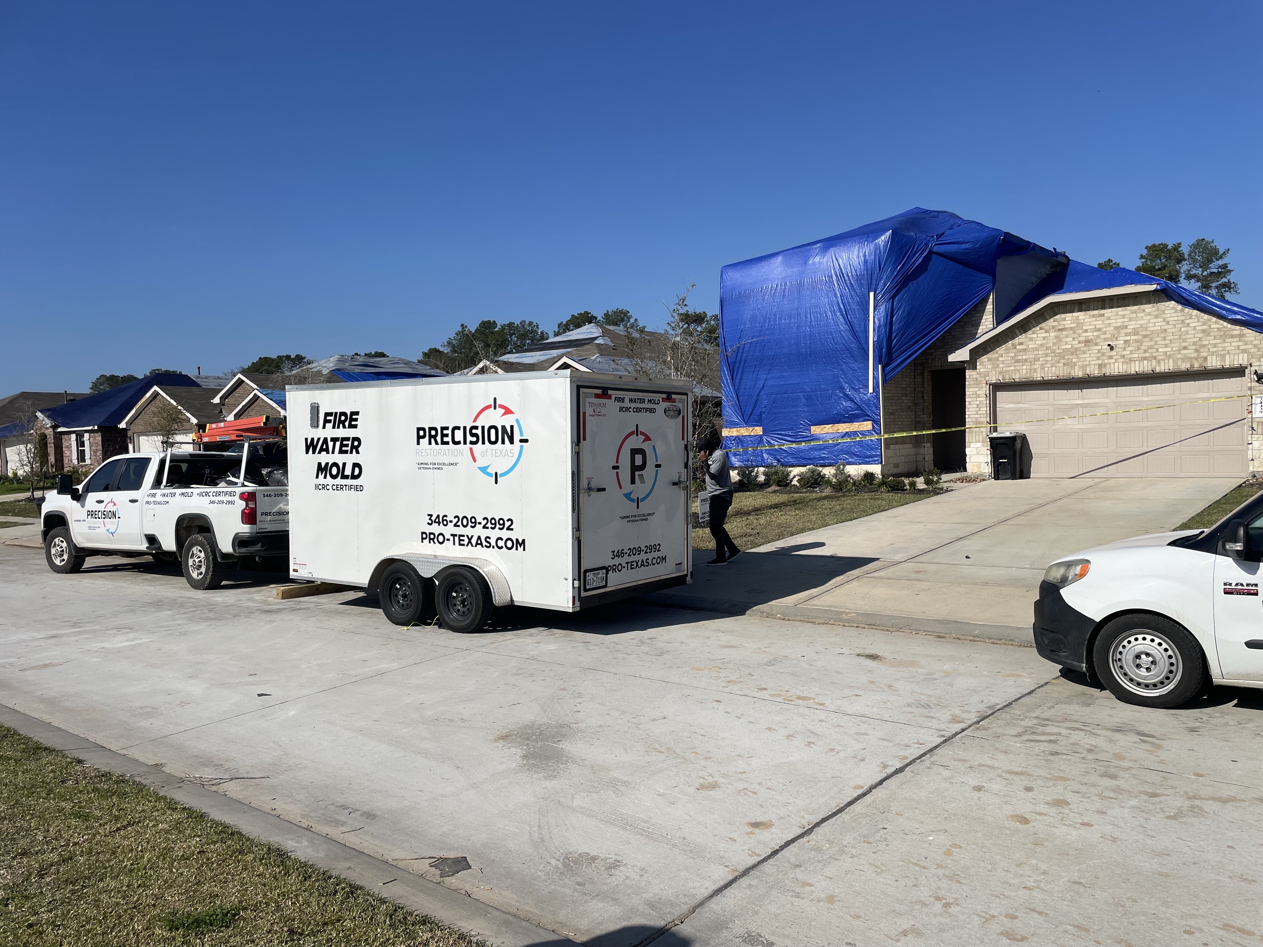 House covered with blue tarps and caution tape, with a restoration truck and trailer parked outside.