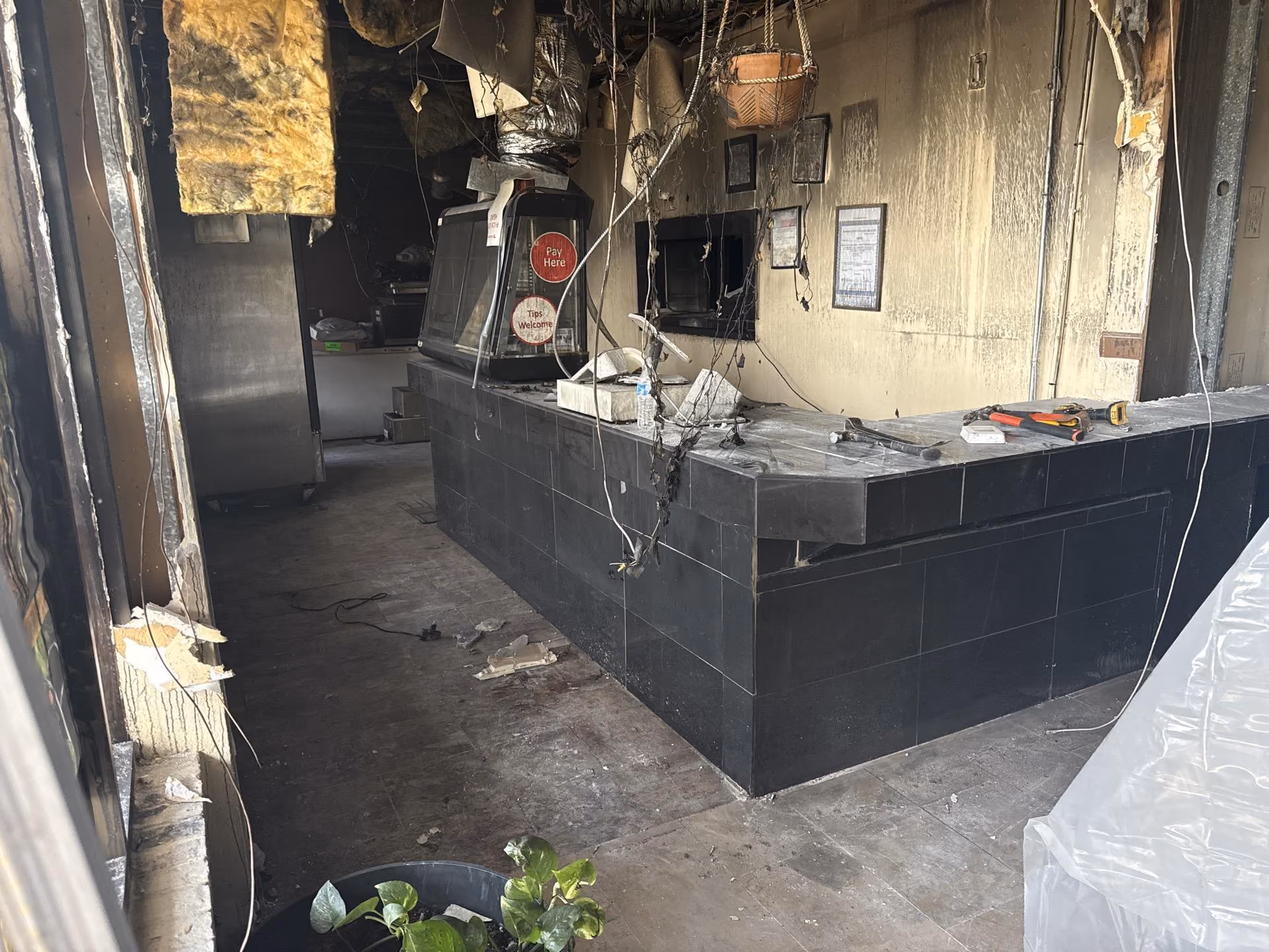 Interior of a fire-damaged commercial kitchen or counter area with hanging wires and debris.