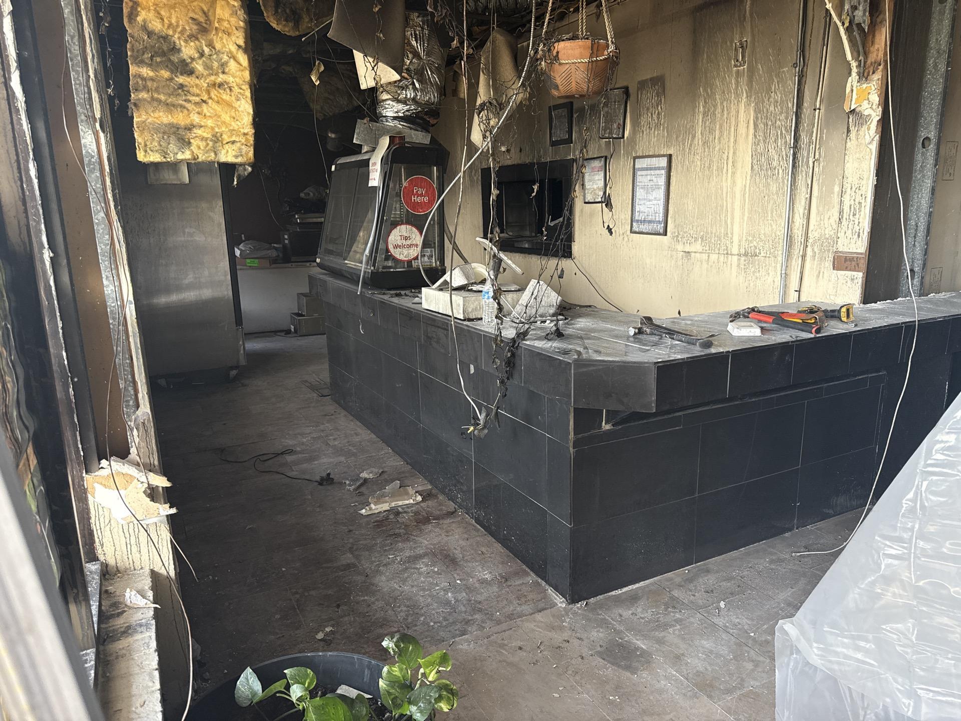 Interior of a fire-damaged commercial kitchen or counter area with hanging wires and debris.