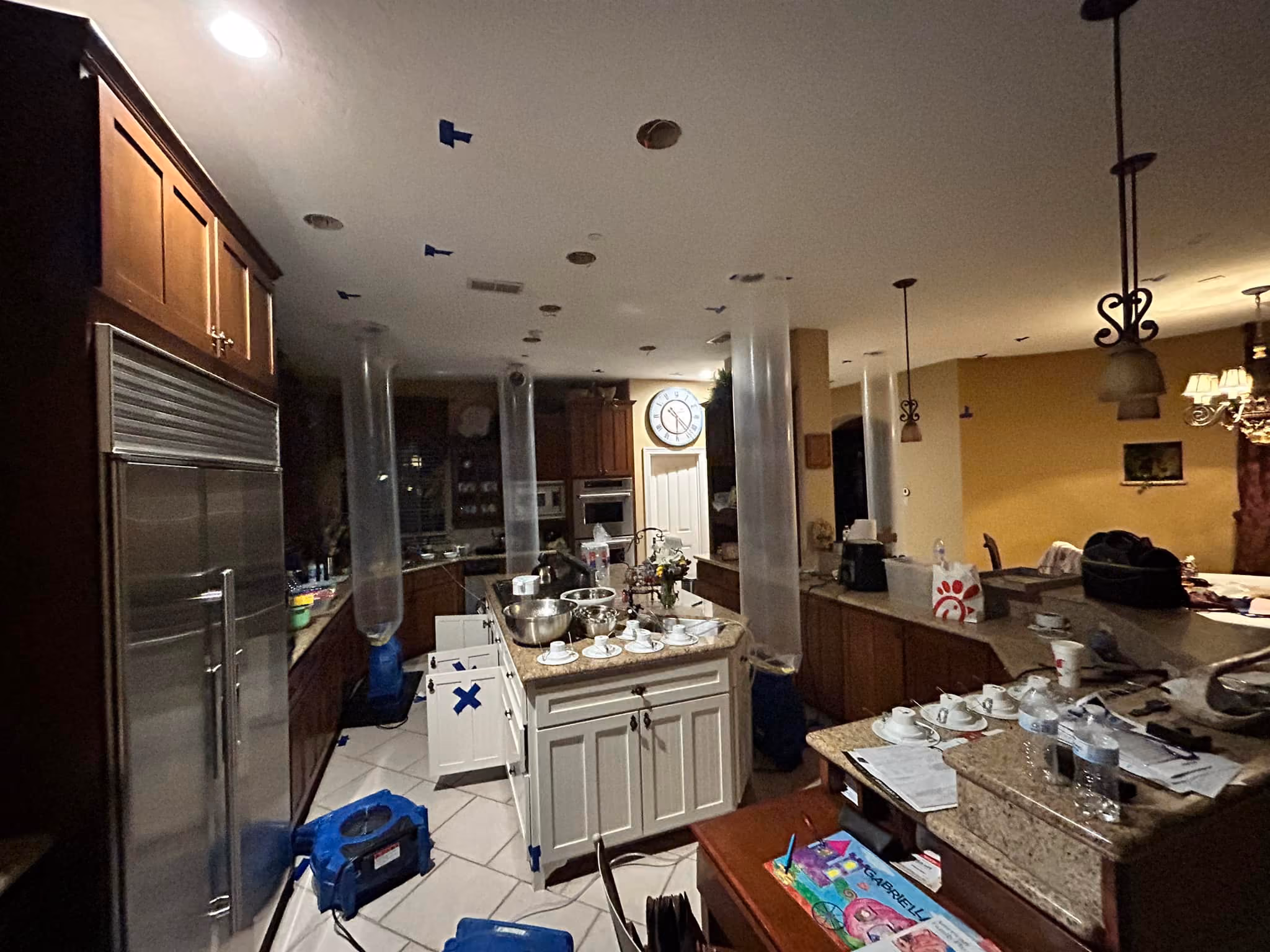 Kitchen with cabinets, appliance, furniture, and drying equipment with blue tape and plastic tubes.