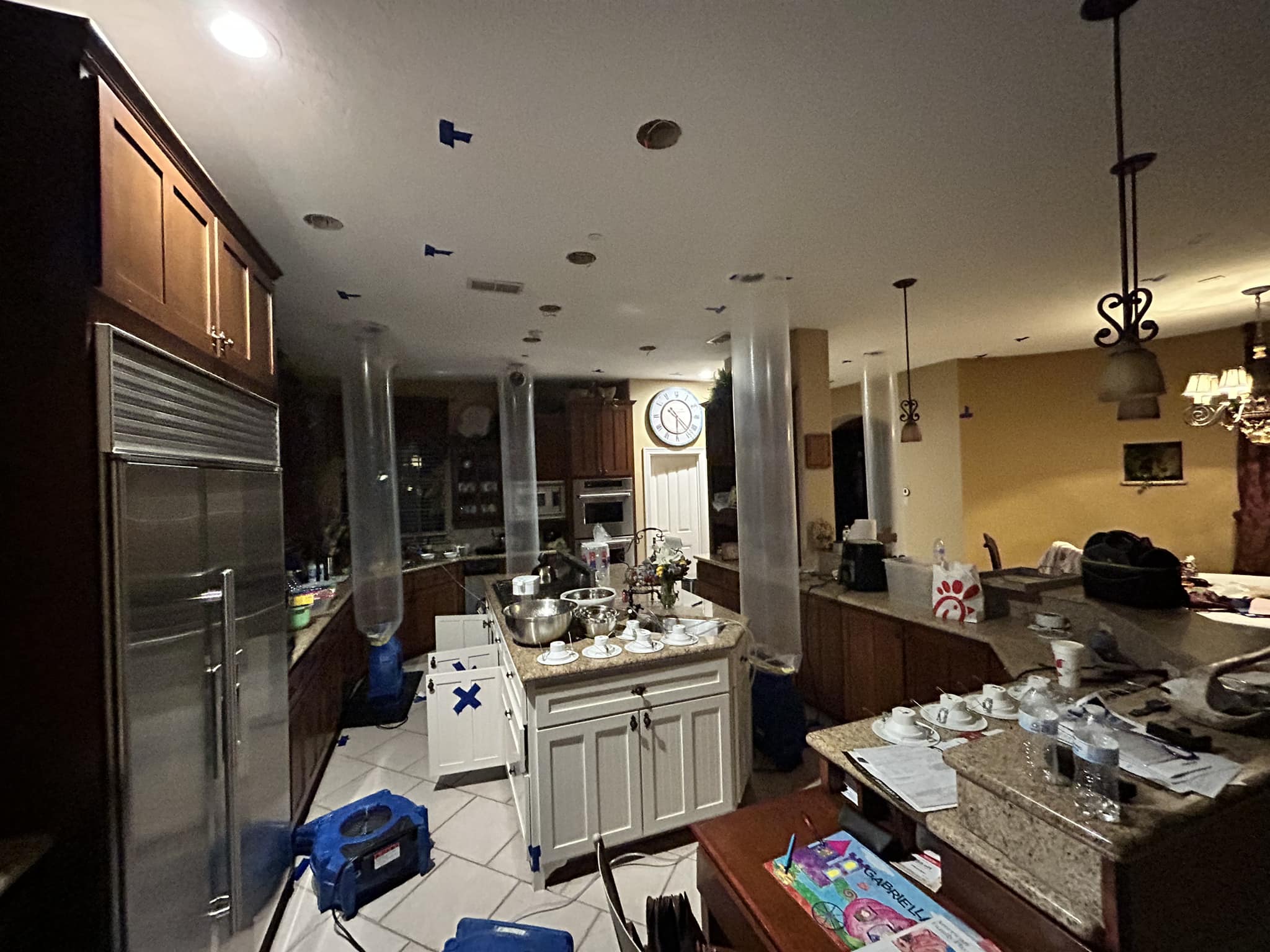 Kitchen with cabinets, appliance, furniture, and drying equipment with blue tape and plastic tubes.