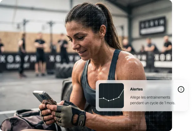 Femme musclée dans une salle de sport regardant son téléphone, épuisée après un entraînement.