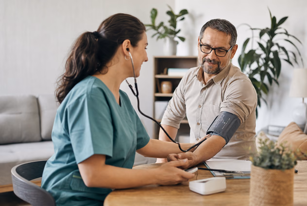 Healthcare worker in green scrubs measuring a middle-aged man's blood pressure indoors.