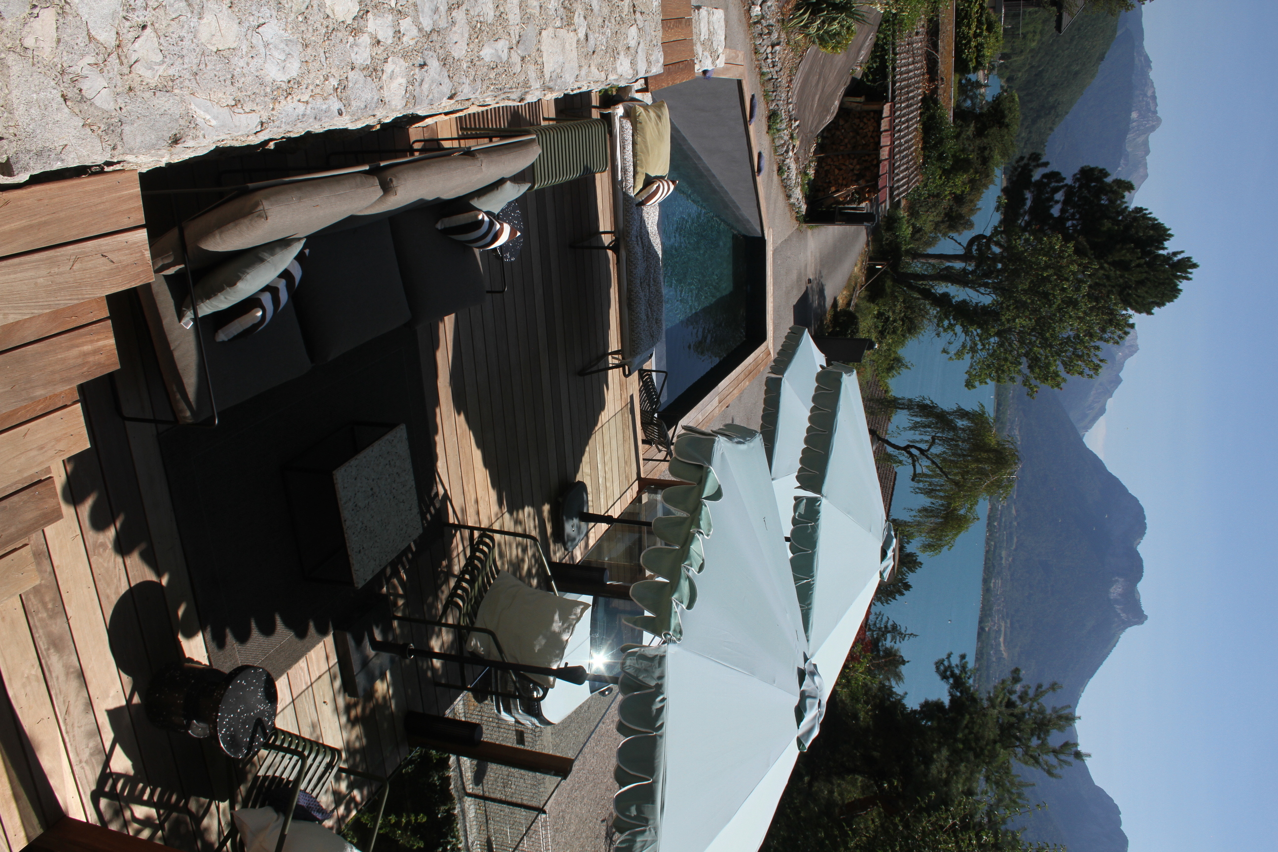 Aménagement extérieur avec mur en pierre, parasols et vue sur le lac.