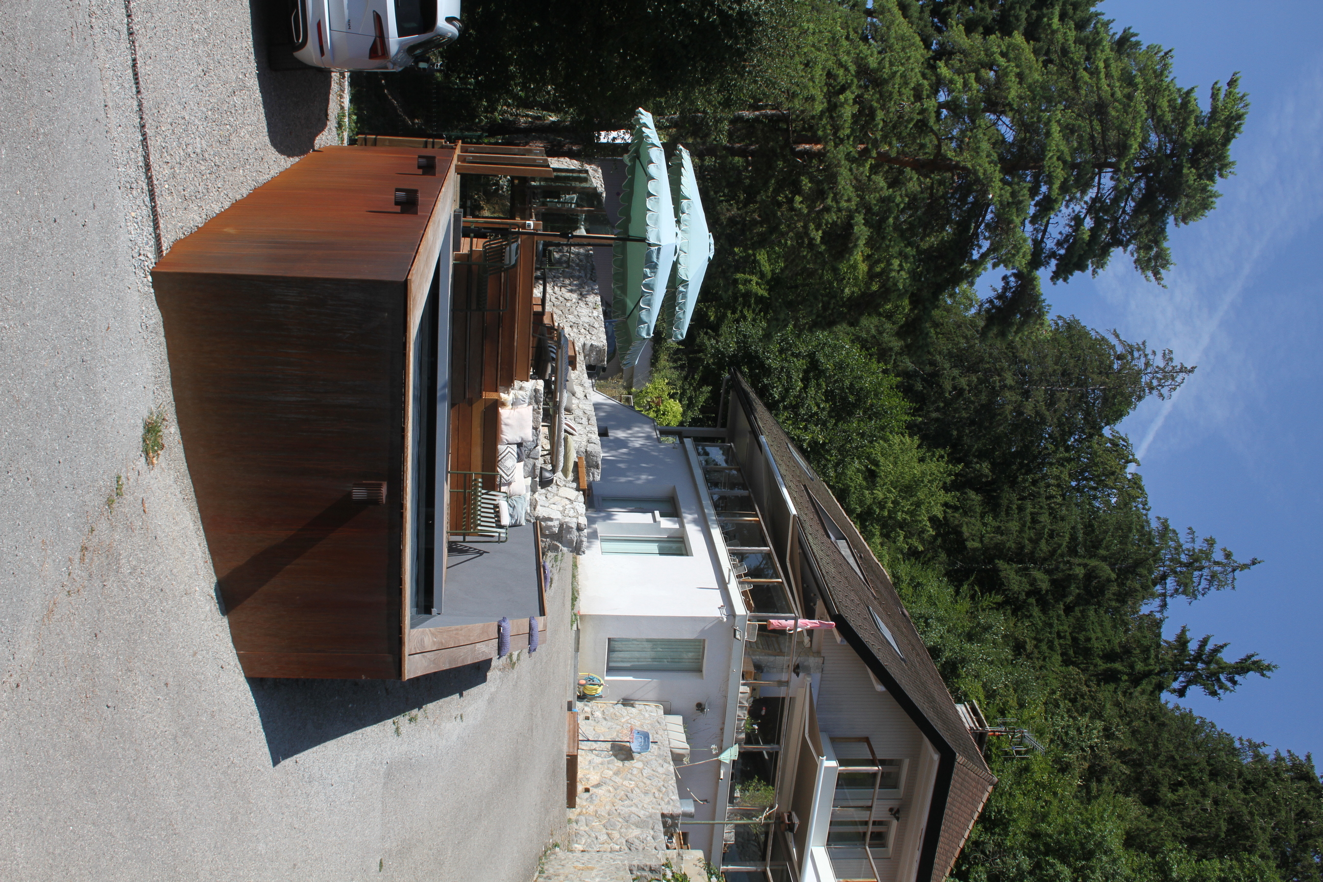 Vue en plongée sur l'espace terrasse en bois, la piscine et le paysage.