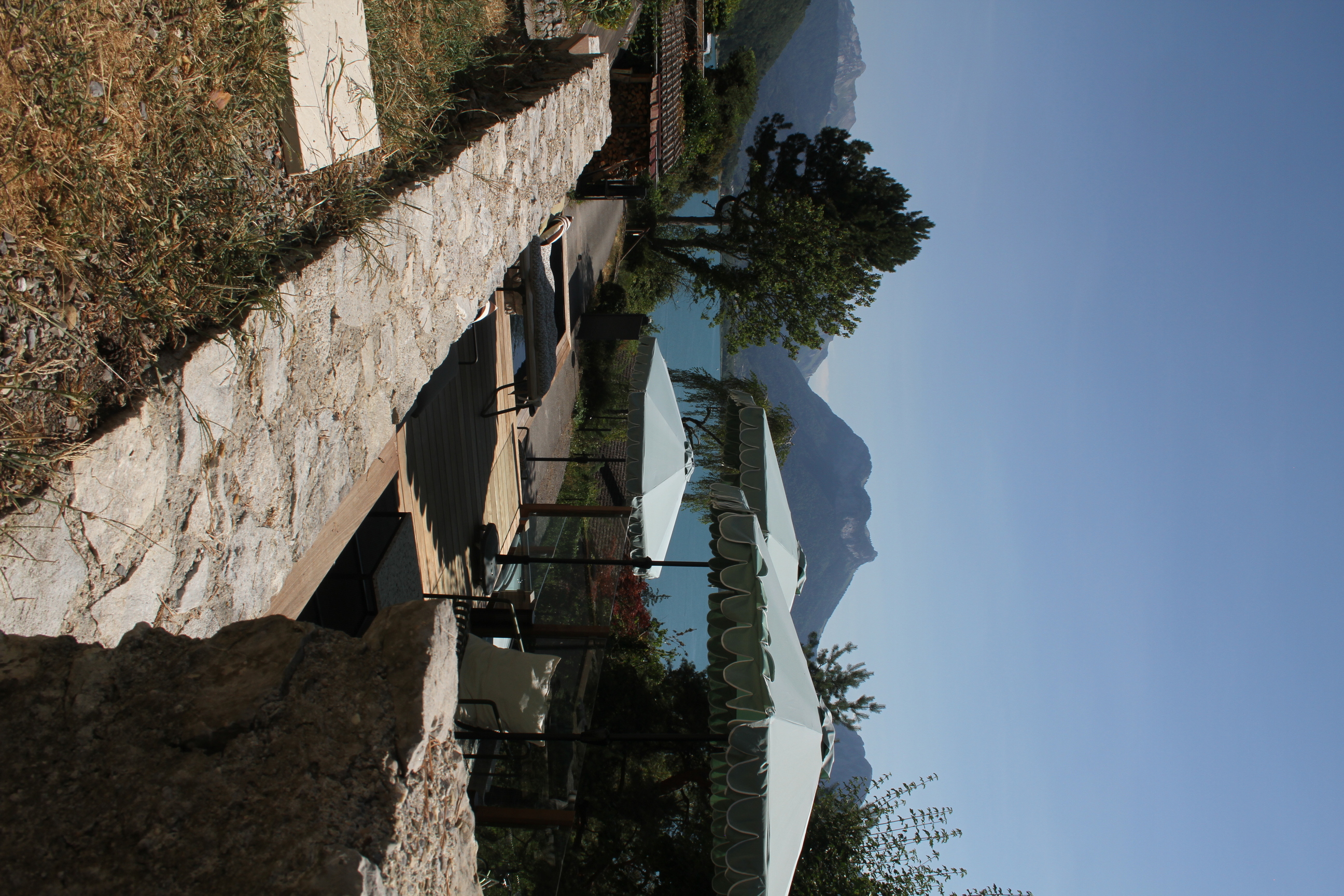 Terrasse paysagée avec mur en pierre et vue panoramique sur le lac et les montagnes.