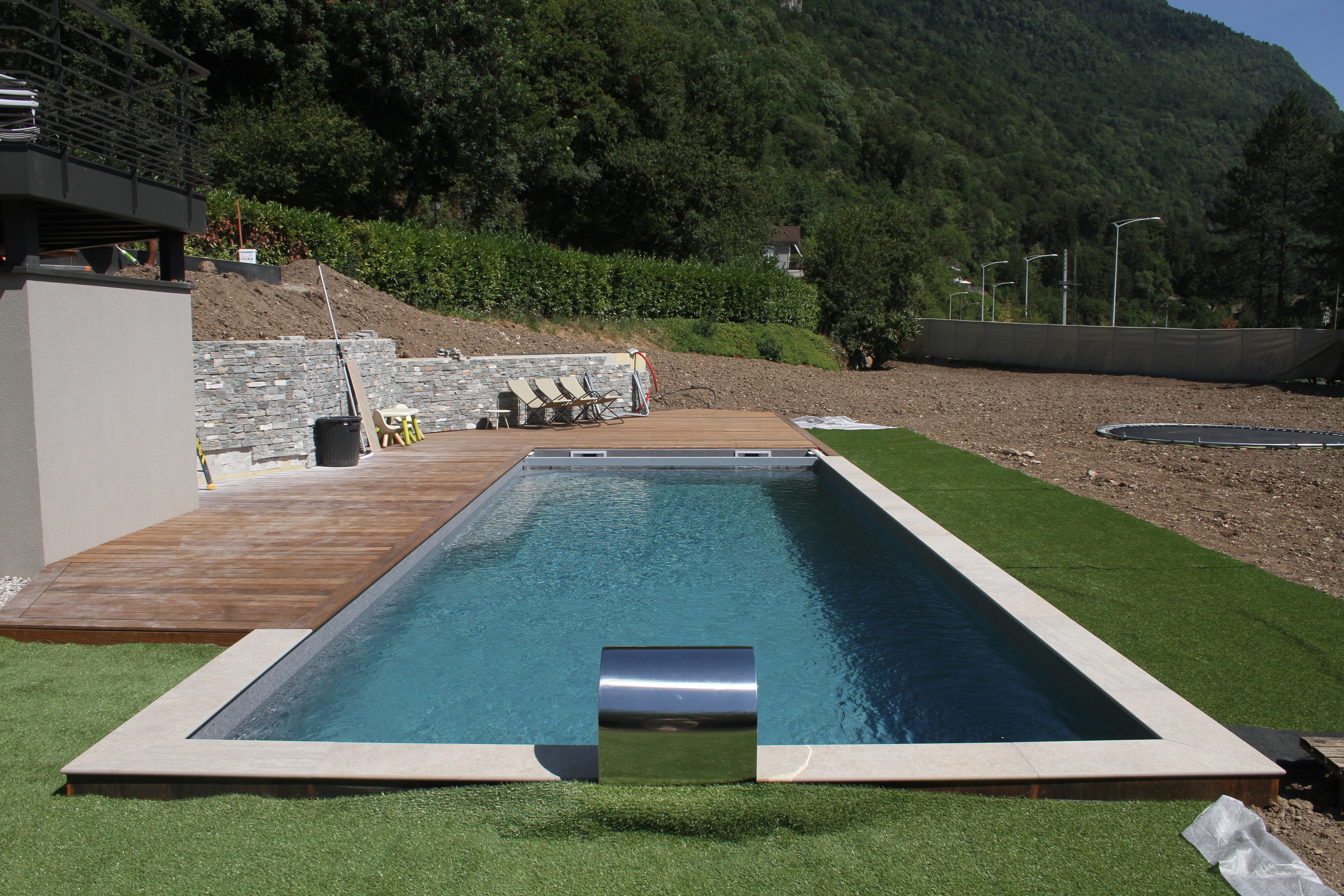 Bassin de piscine rectangulaire entouré d'une terrasse en bois et d'une pelouse.