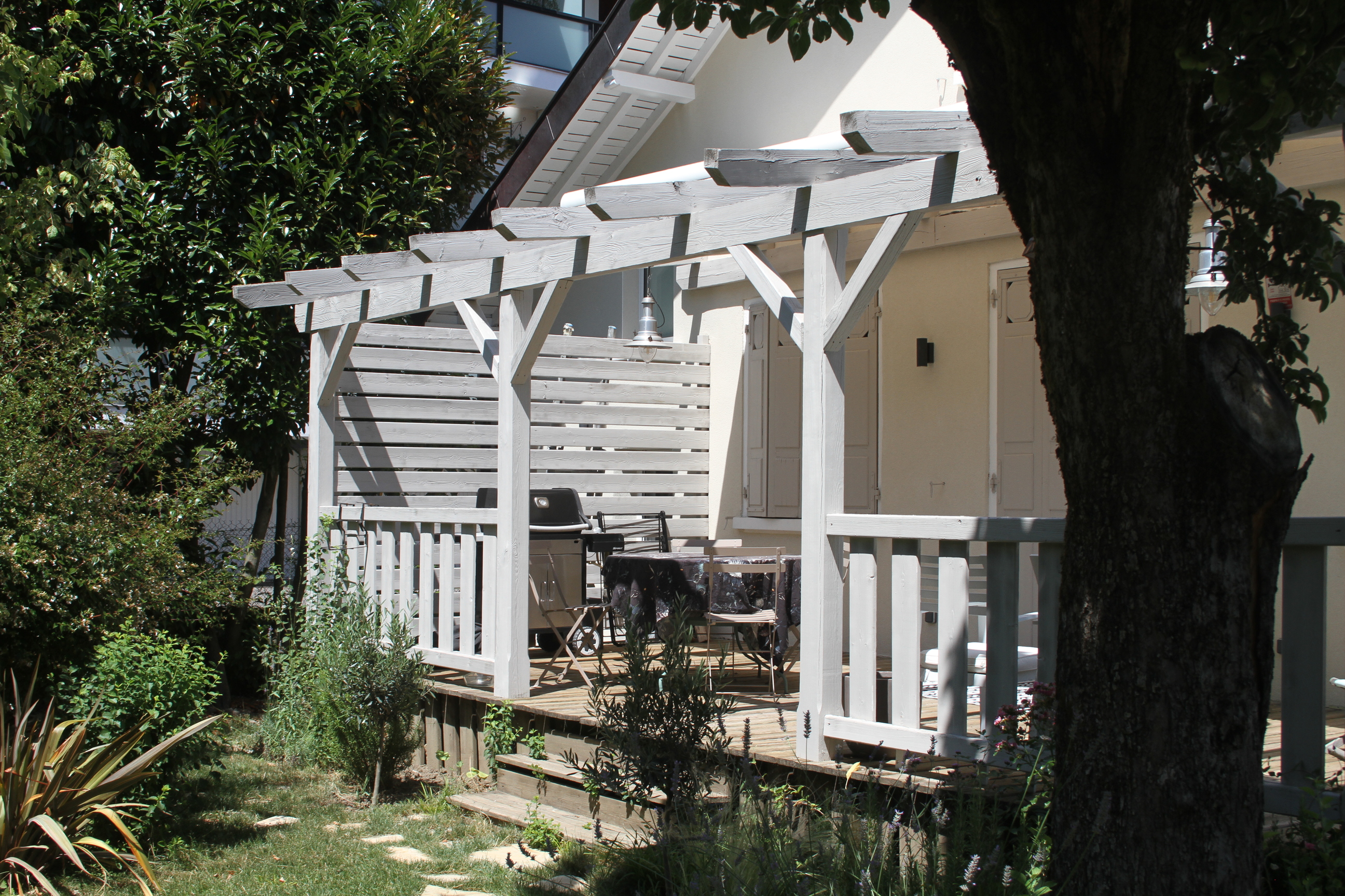 Façade principale de la maison avec pergola en bois et jardin arboré.