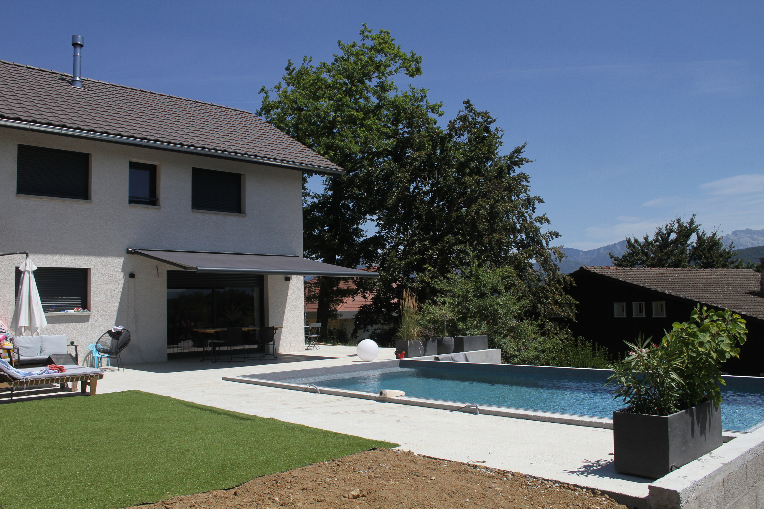 Maison contemporaine avec piscine, grande terrasse en béton et store banne déplié.