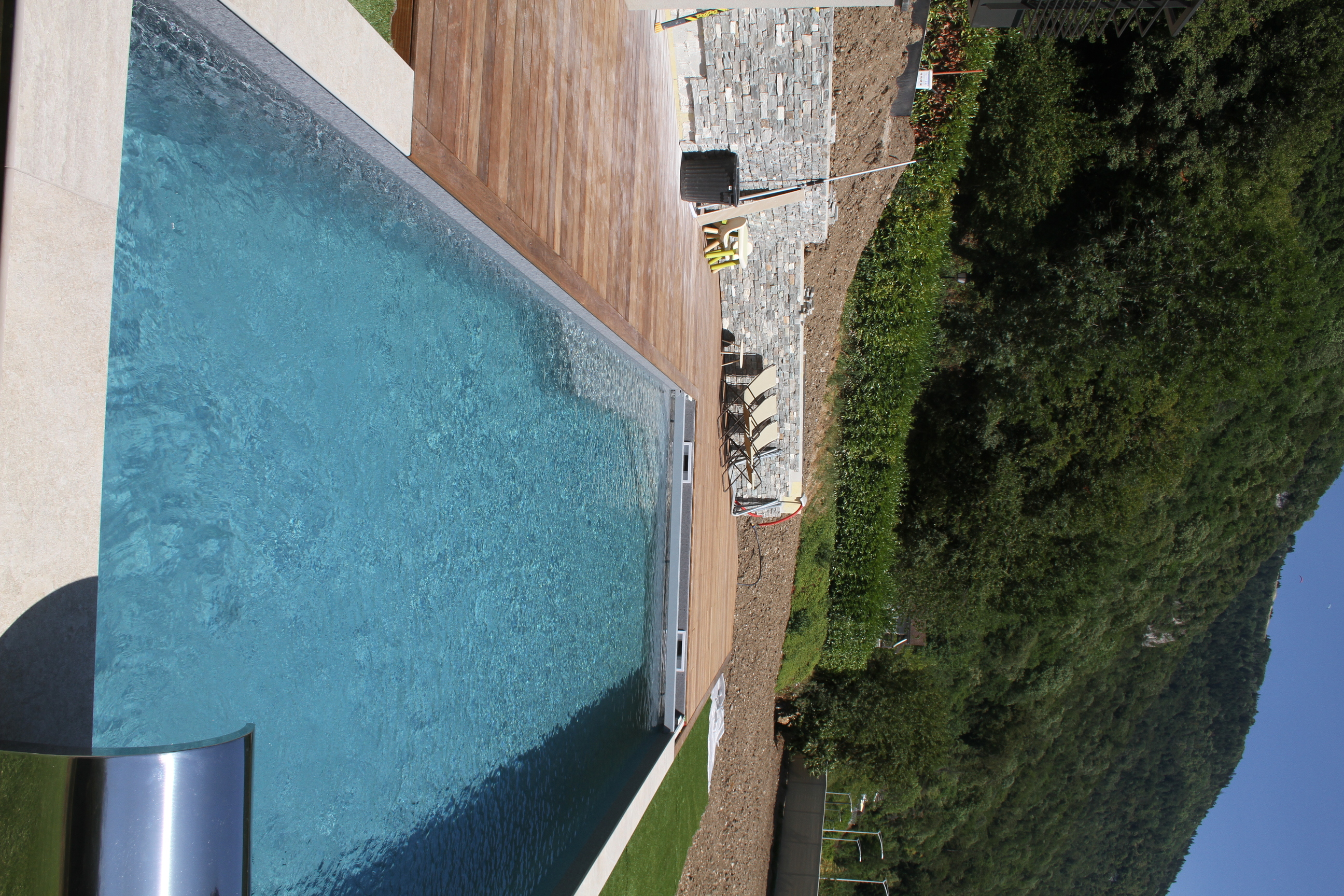 Piscine rectangulaire avec plage en bois située au pied d'une montagne.