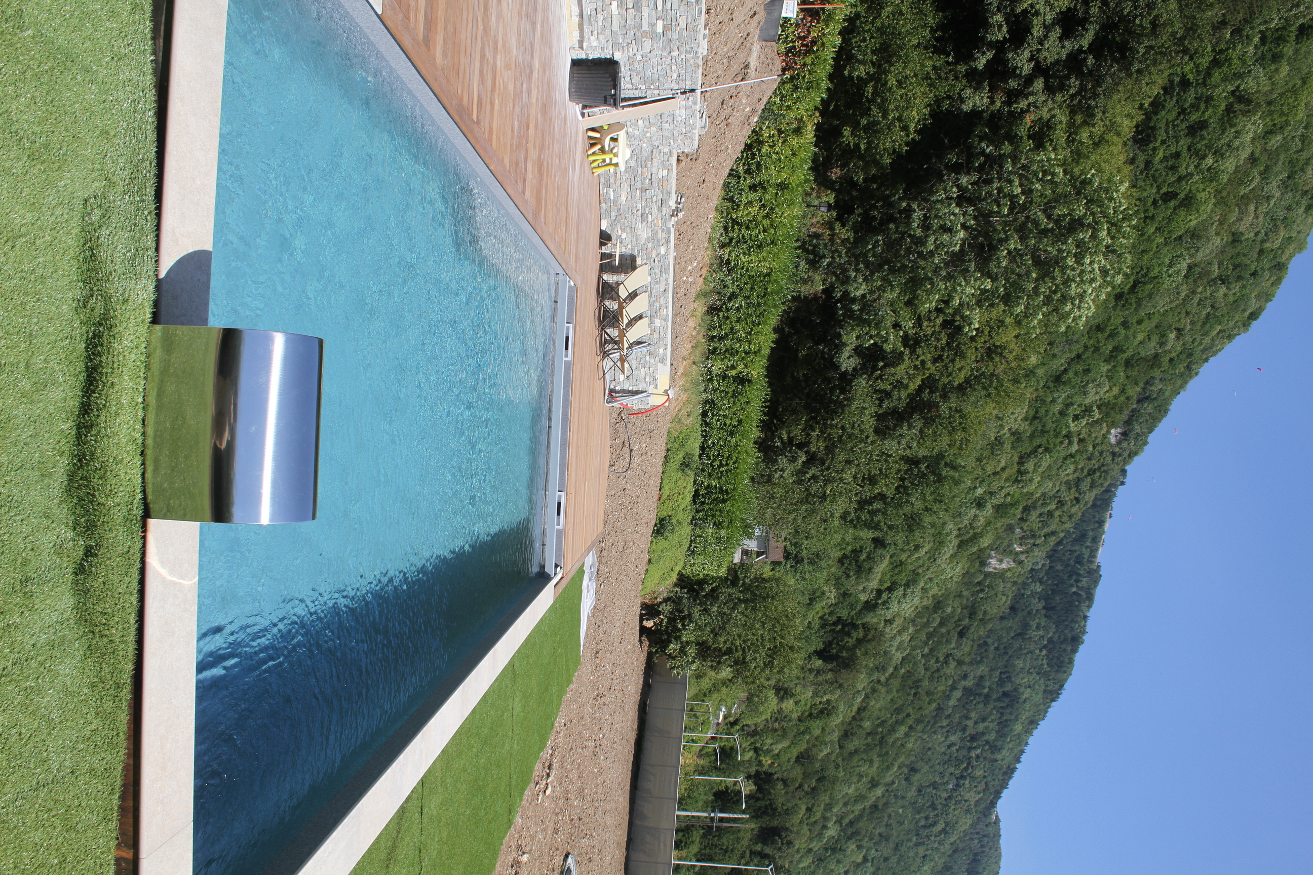 Vue dans l'axe d'une piscine rectangulaire avec cascade en inox et environnement montagneux.