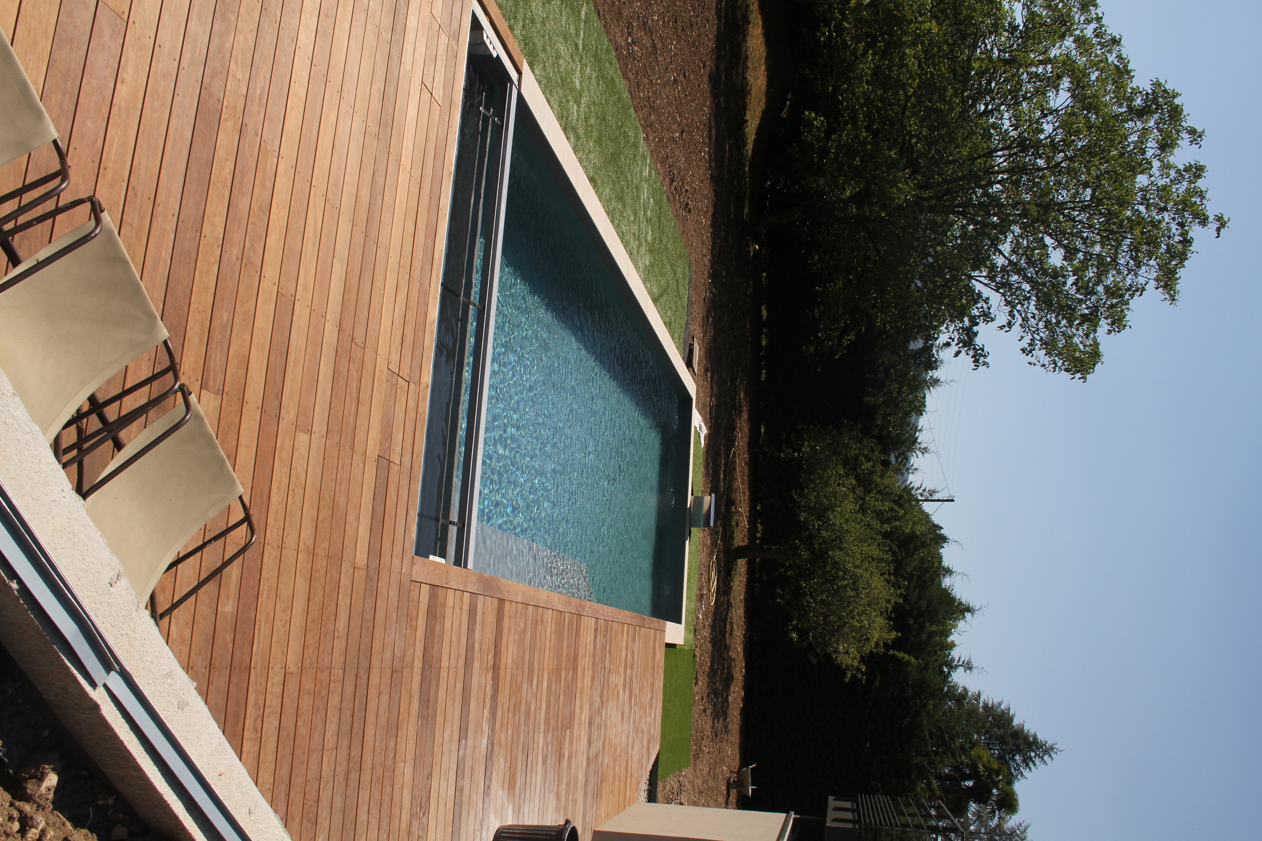 Vue plongeante d'une piscine avec volet roulant immergé ouvert et grande terrasse en bois.