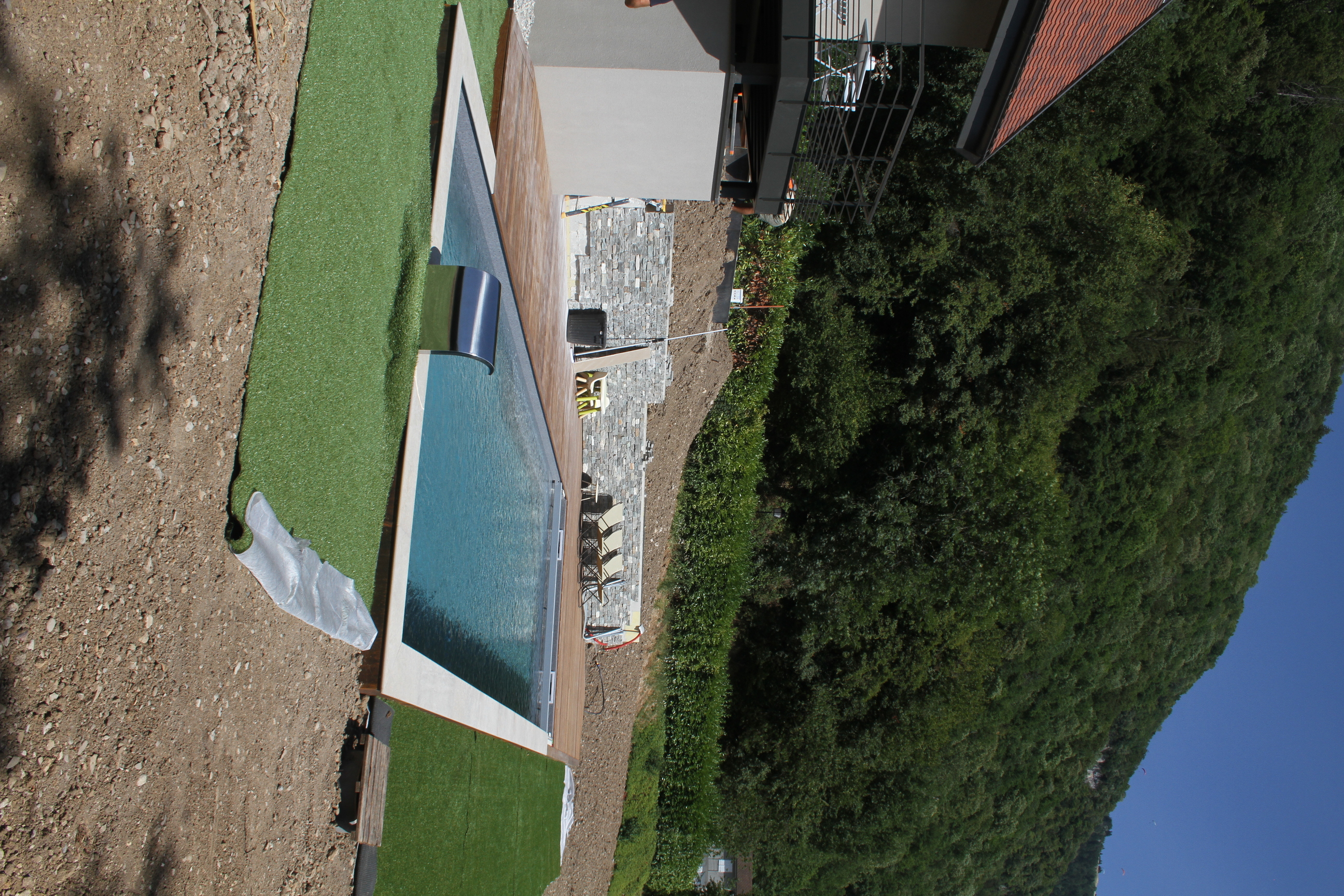 Vue globale de l'aménagement extérieur avec piscine, terrasse en bois et gazon synthétique.