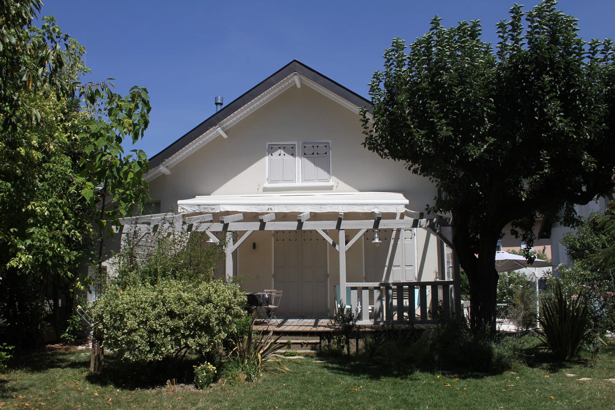 Façade principale de la maison avec pergola en bois et jardin arboré.
