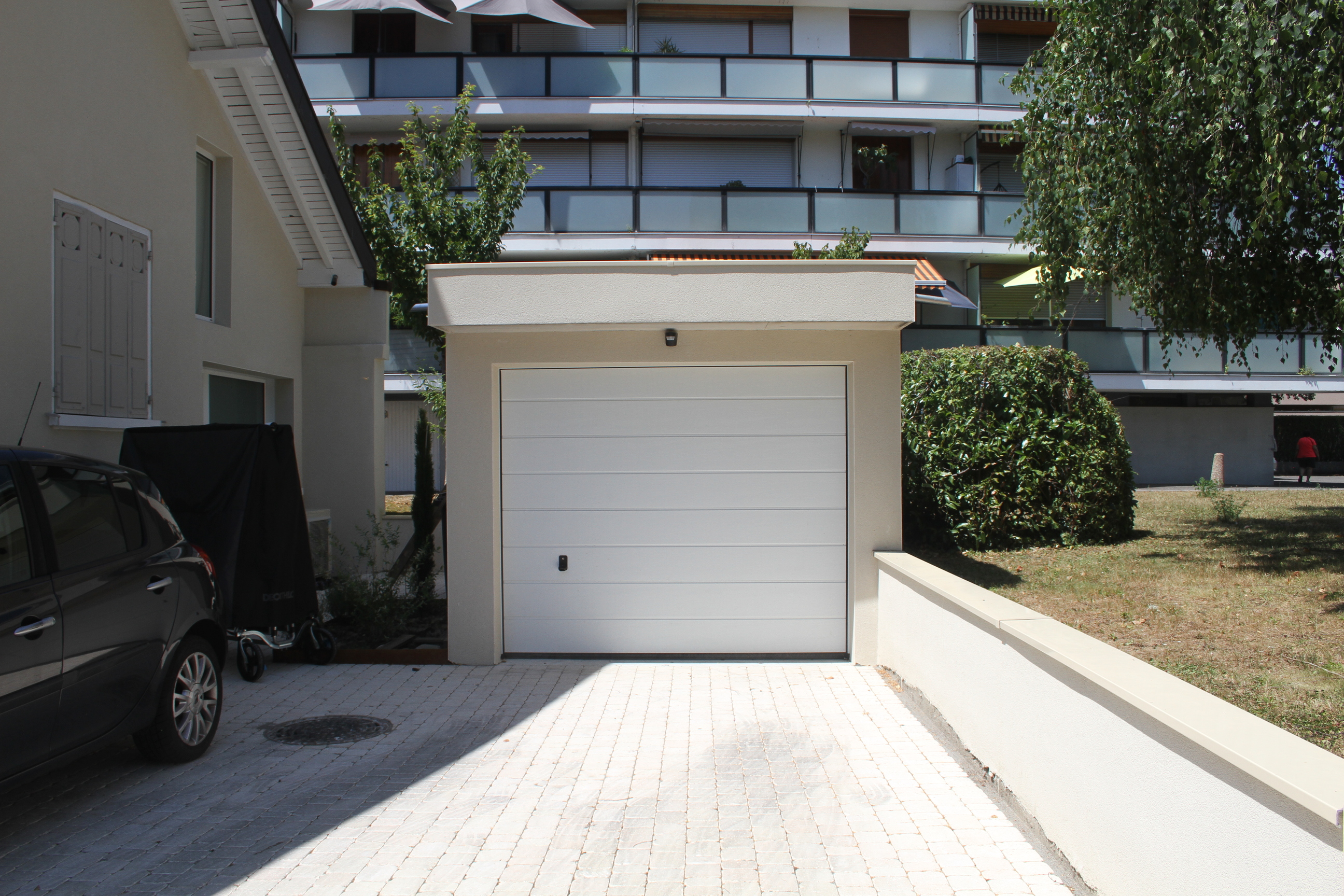 Allée pavée menant au garage avec aperçu de la façade et d'un véhicule.