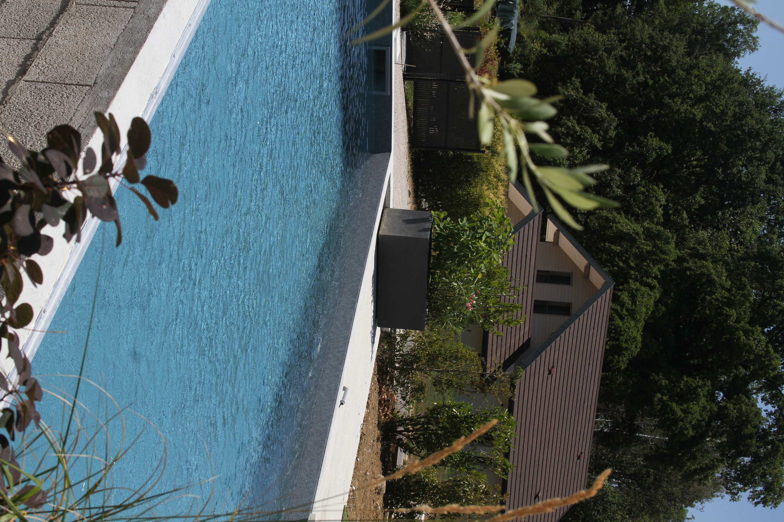 Vue partielle d'une piscine creusée avec une maison individuelle en arrière-plan.