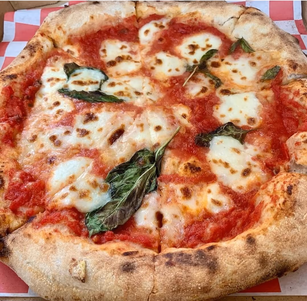 Person spreading red tomato sauce on pizza dough on a floured countertop in a kitchen.