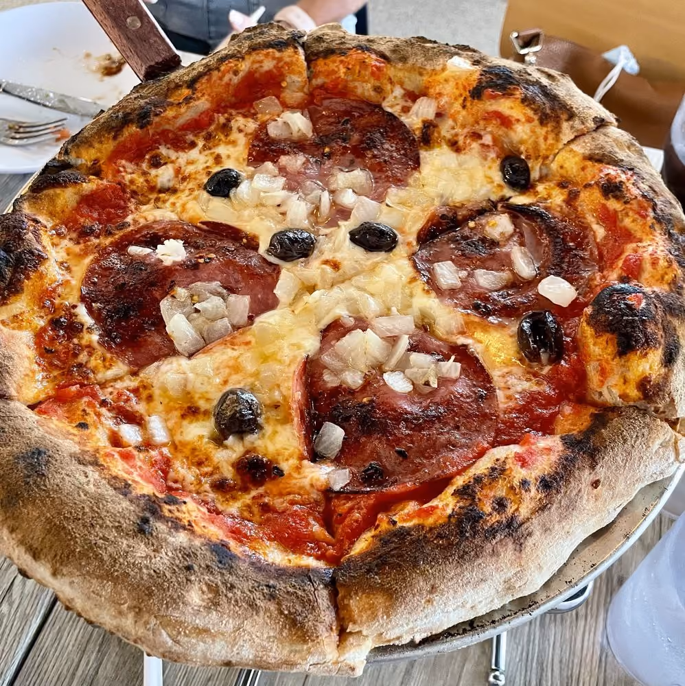 Close-up of a pepperoni pizza with black olives and diced onions on a wood-fired crust.