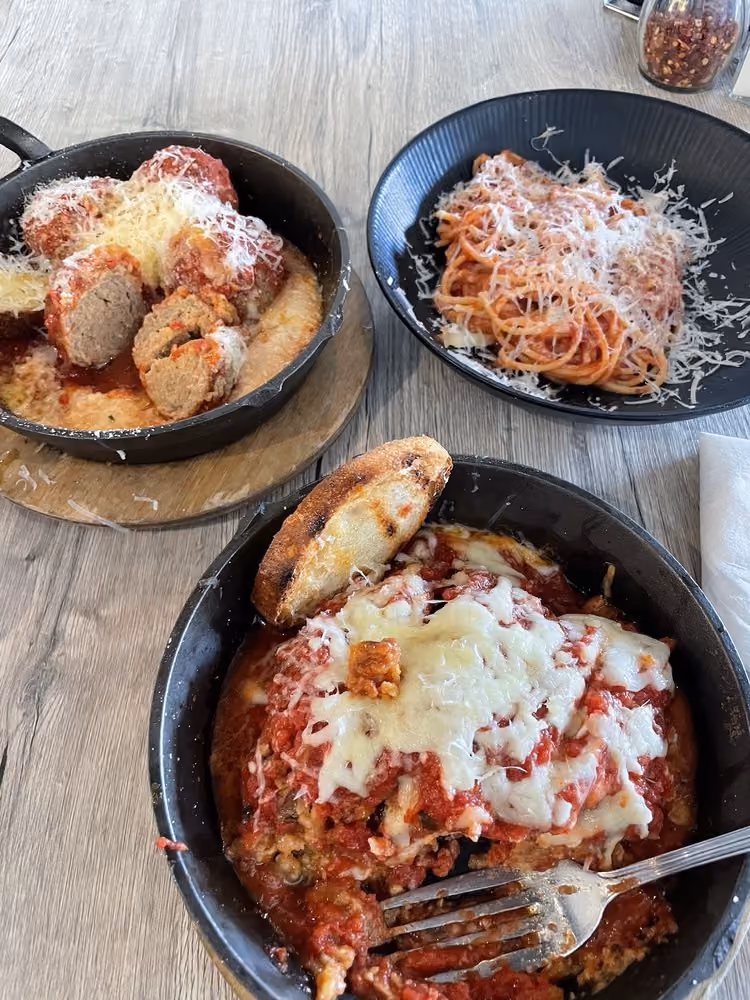 Top view of three Italian dishes: meatballs with sauce, spaghetti with cheese, and baked lasagna with bread.
