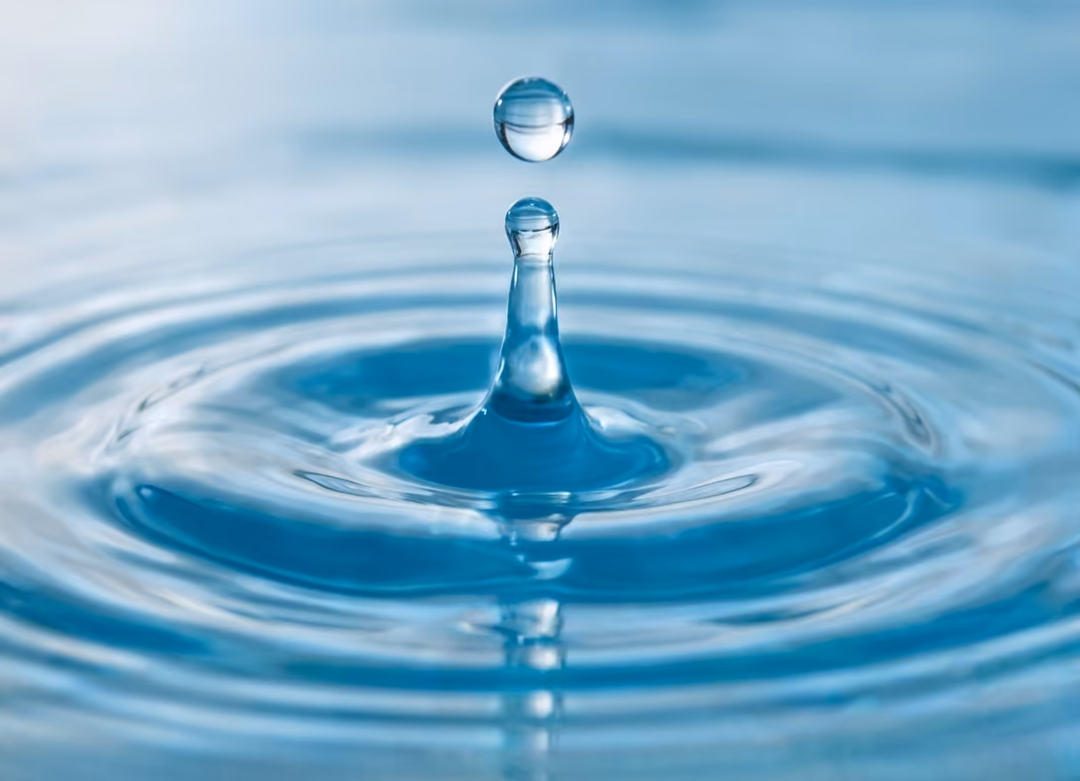 Close-up of a water droplet suspended above rippling blue water surface.