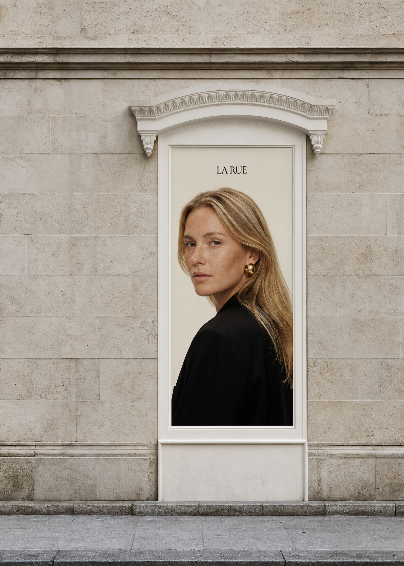 Billboard on stone wall showing a portrait of a blonde woman with freckles, wearing a black top and large gold hoop earrings, looking over her shoulder, with the text 'LA RUE' above her head.