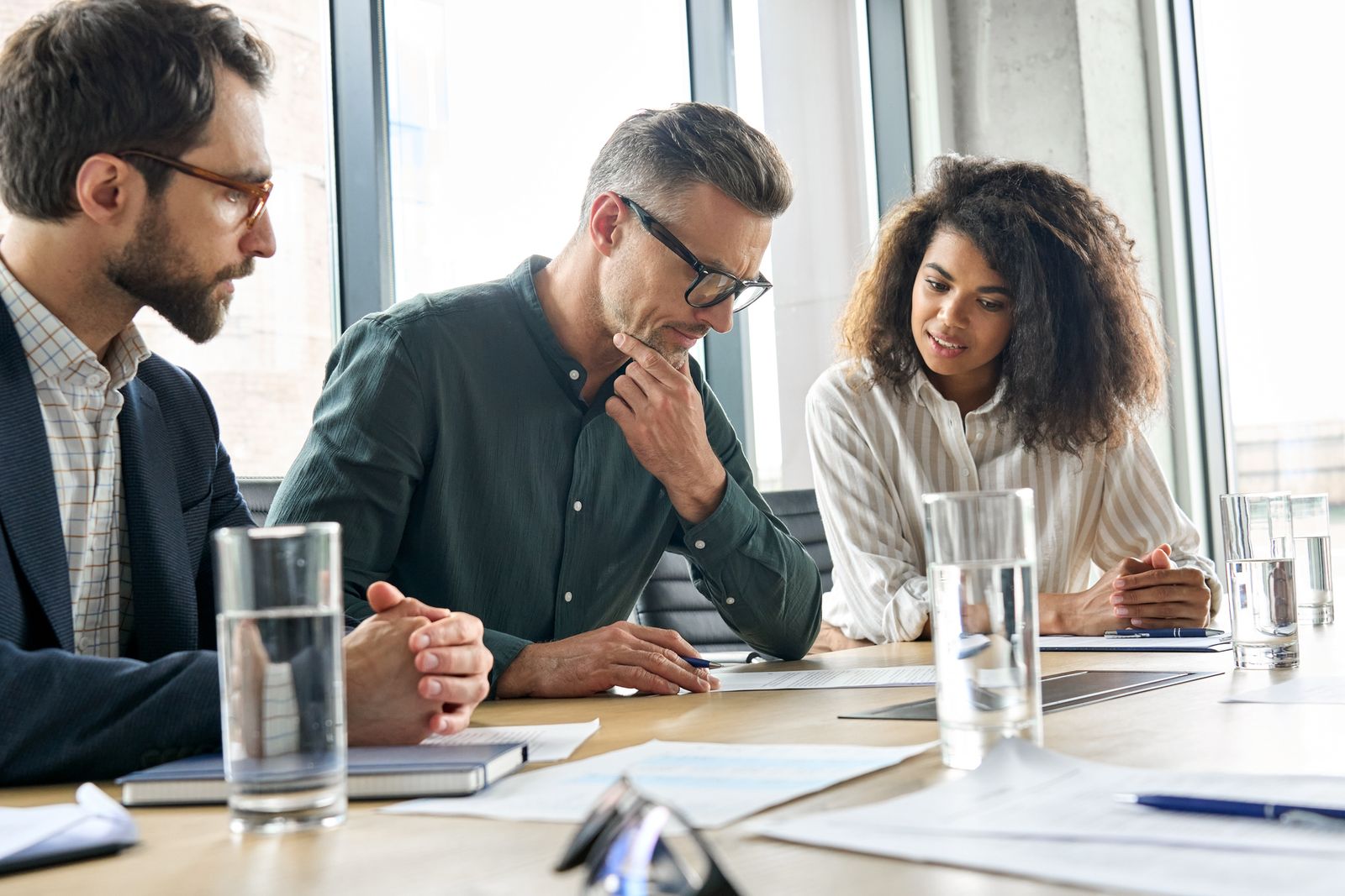 Three colleagues reading a document together at a boardroom table