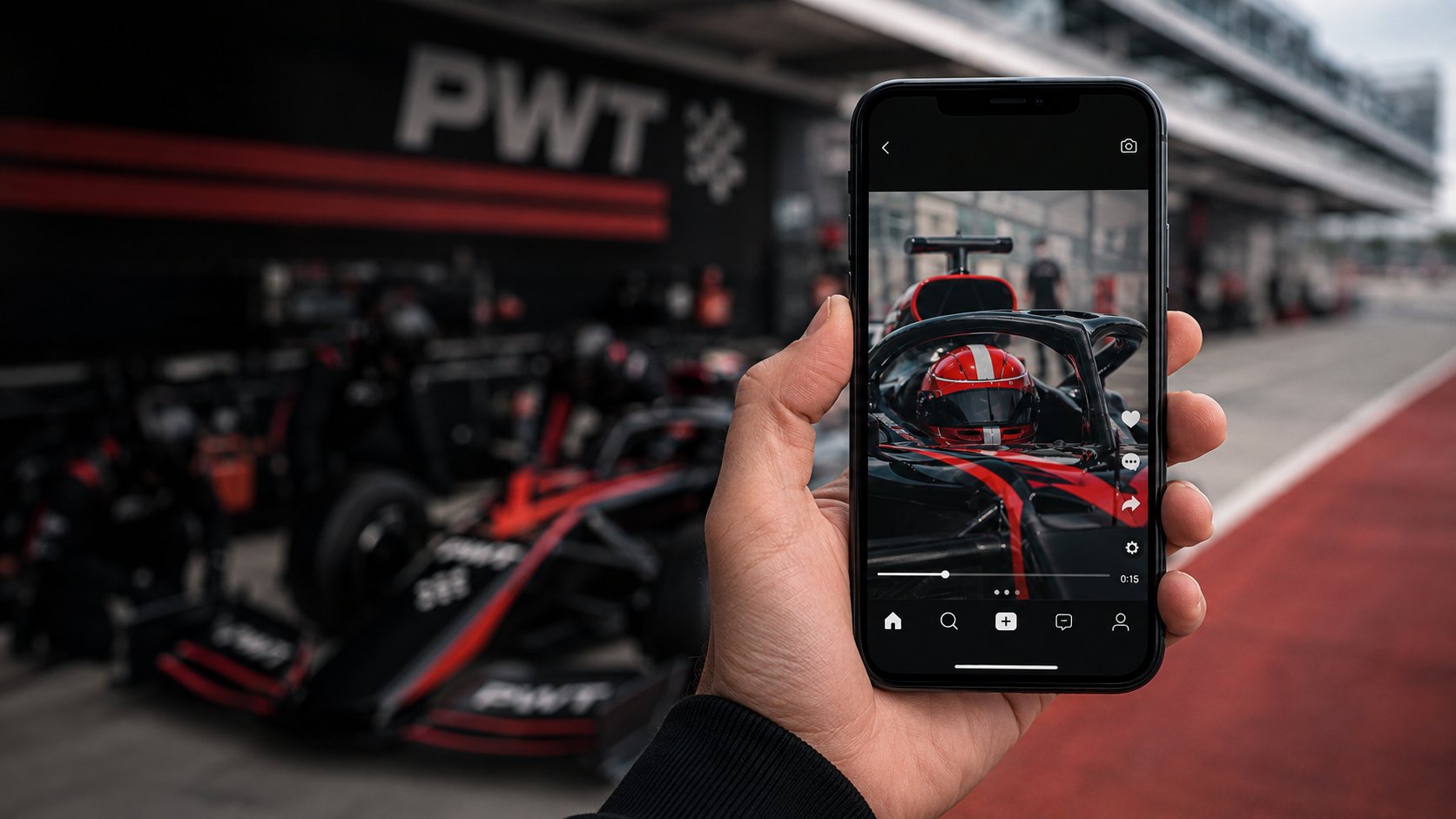 A phone held up in the pit lane playing a short clip of a PWT car, the garage behind it.