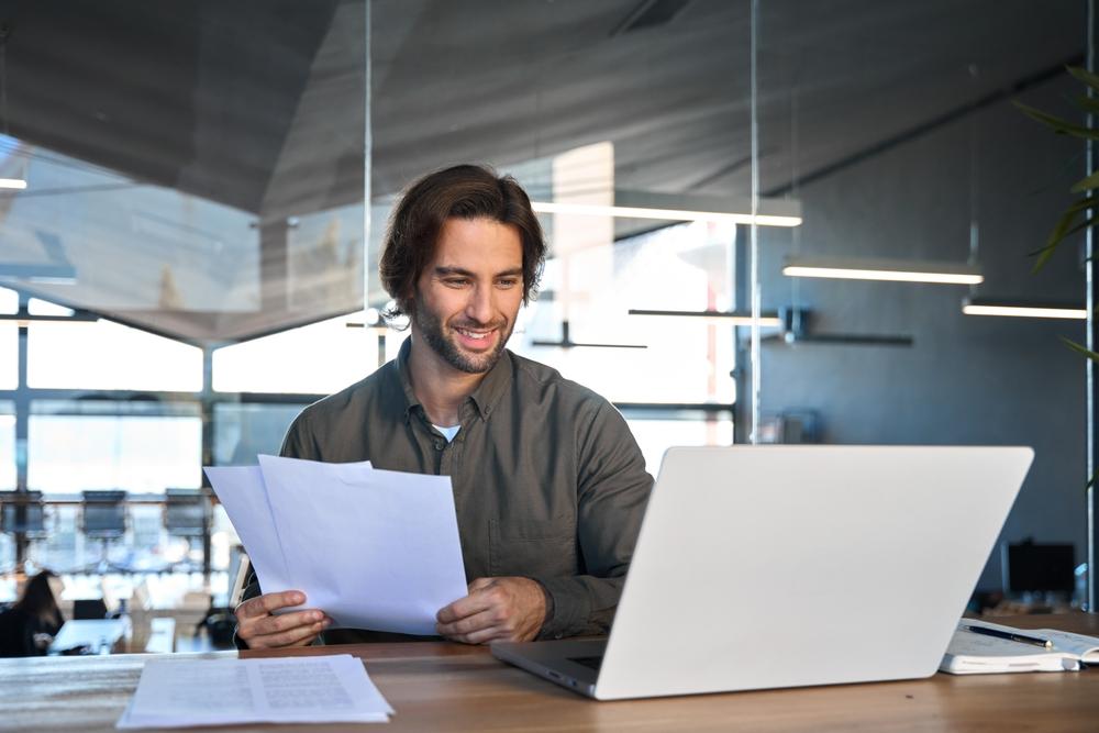 A small business owner comparing documents to a laptop.