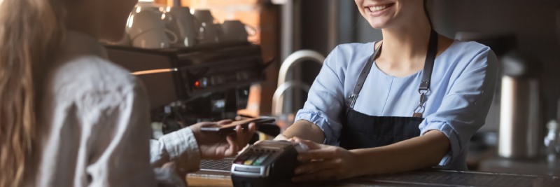 A coffee shop employee holds out a terminal for a customer to make a credit card payment.