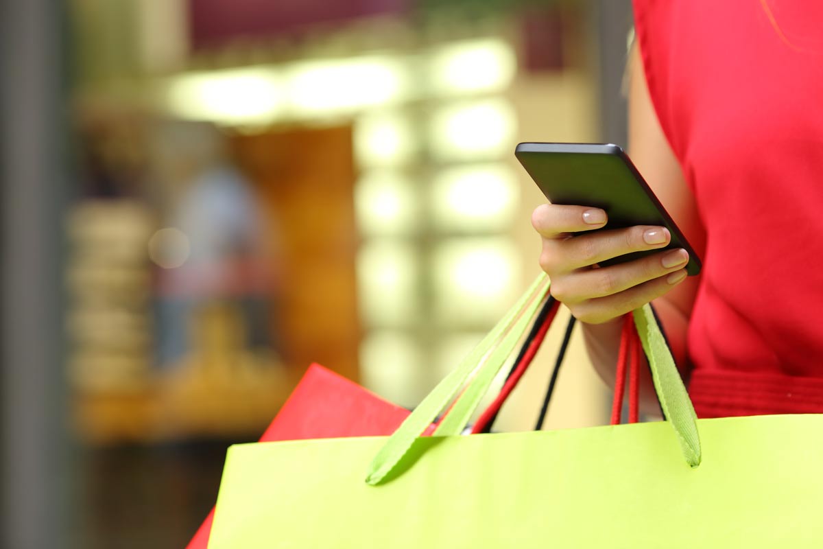 A customer uses a smartphone while holding two shopping bags.