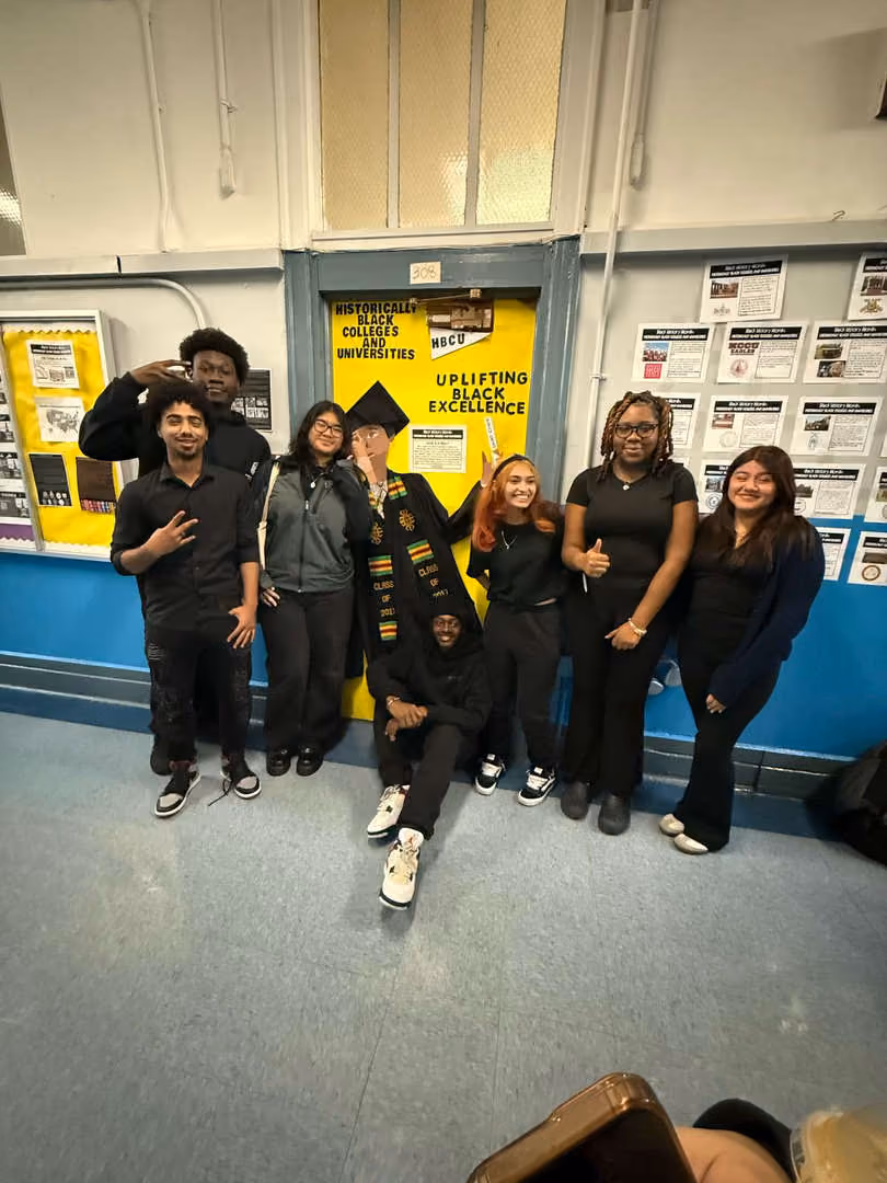 Students pose by HBCU bulletin board with graduate in cap and stole
