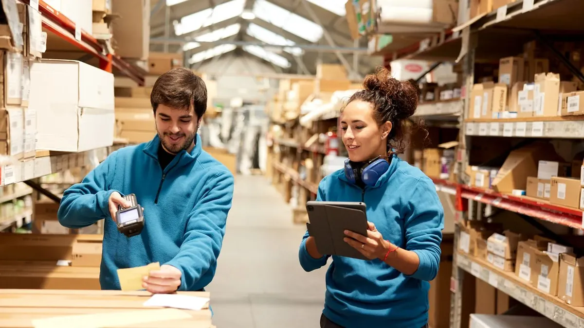 Two workers counting stock in a racking aisle, one scanning and one checking a tablet