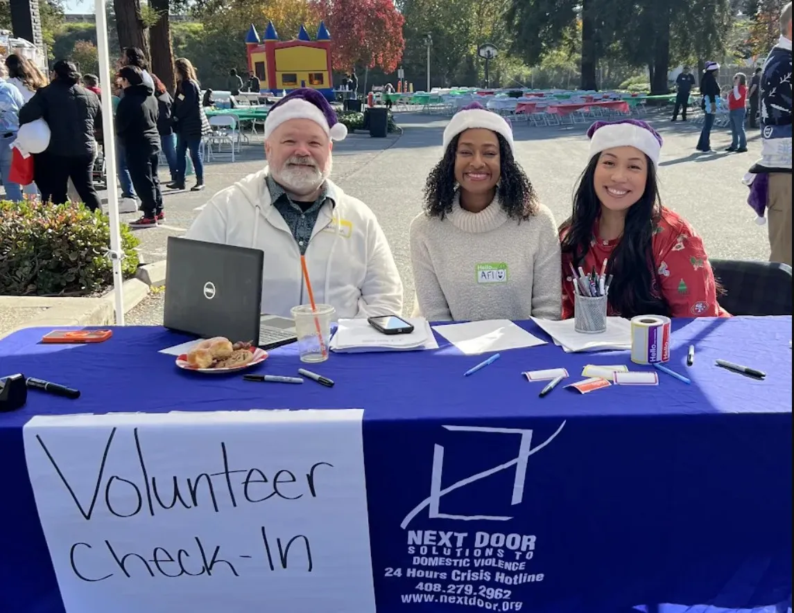 Three volunteers in Santa hats staff the Next Door Solutions volunteer check-in table