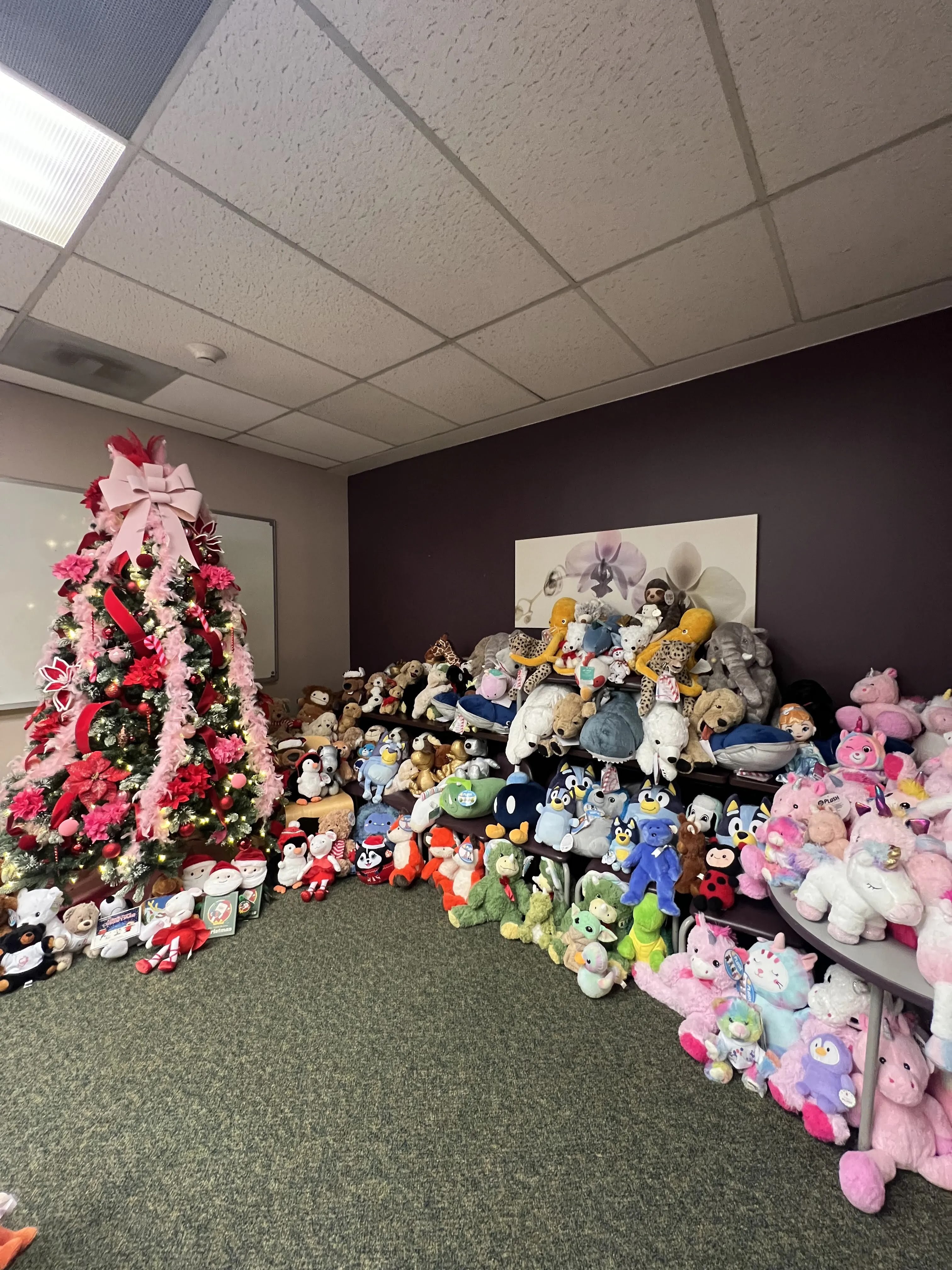 Donated stuffed animals arranged beside a decorated holiday tree
