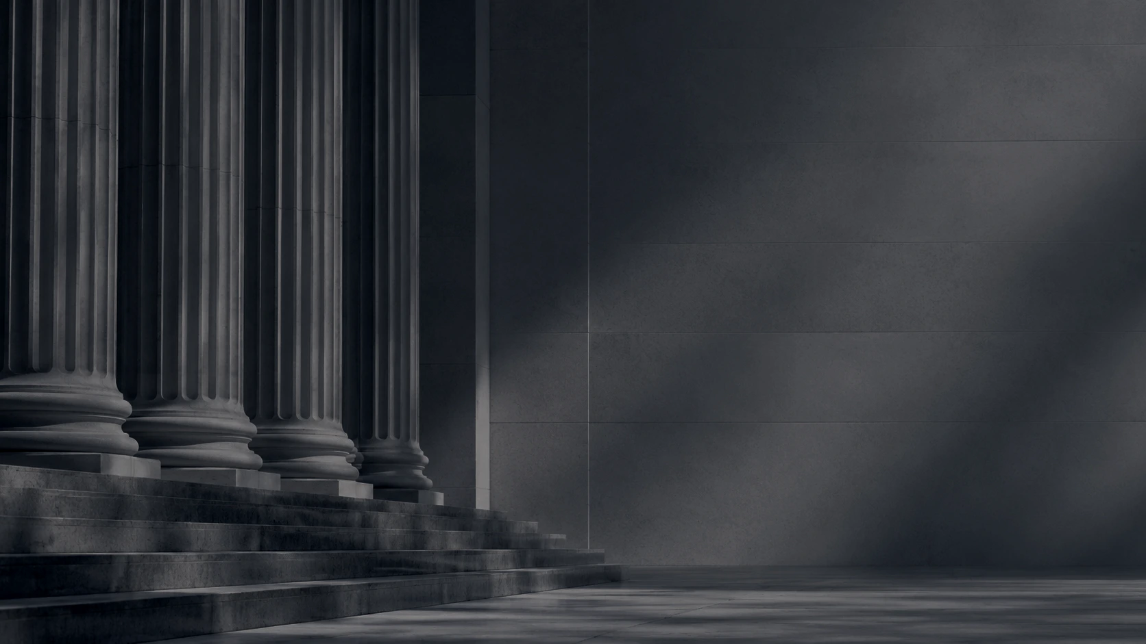 Stone columns outside a courthouse entrance with light and shadows across the walkway