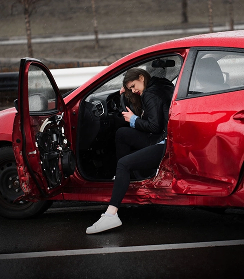 Woman injured after a car crash getting out of a damaged vehicle, illustrating a case for an auto accident attorney in Rego Park
