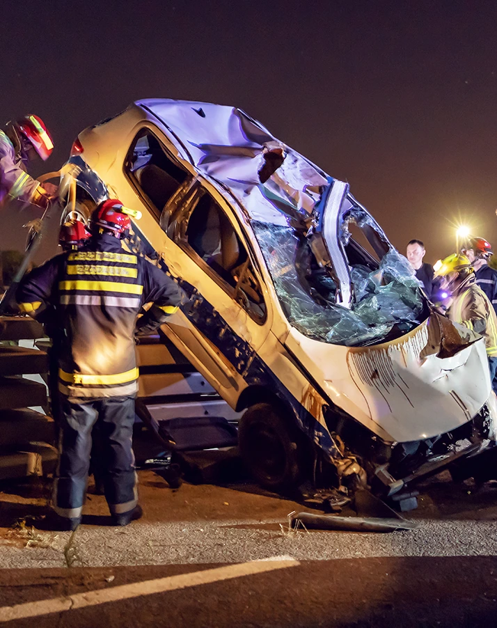 Emergency responders surrounding a badly crushed vehicle after a serious nighttime collision
