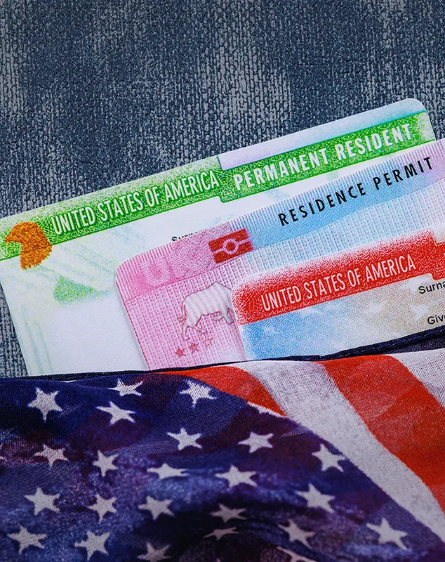 Permanent resident cards beside an American flag, reflecting the stability someone may be working toward with help from a Green Card Attorney in Rego Park