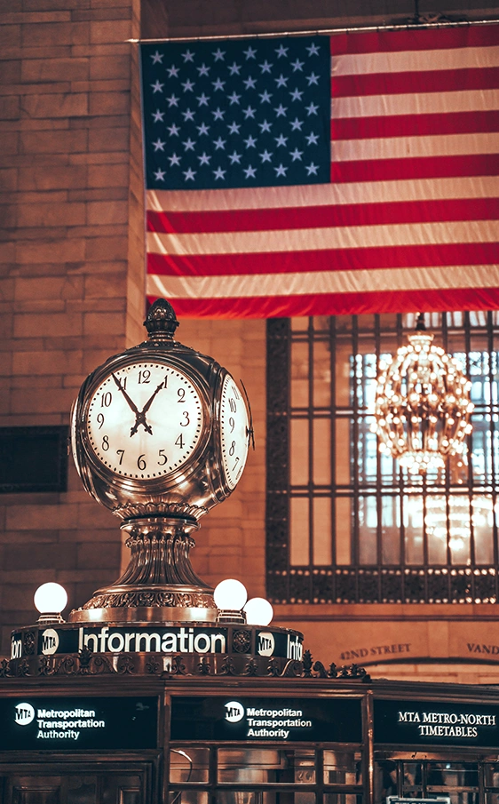 American flag and iconic clock inside Grand Central Terminal, reflecting the life in New York someone may be working to make permanent with help from a Citizenship Lawyer in Rego Park