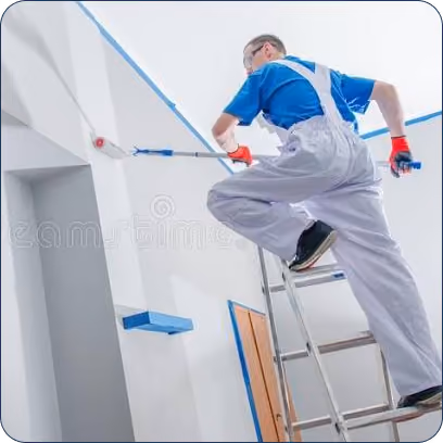 Painter in overalls on ladder uses roller to paint wall near ceiling in white room.