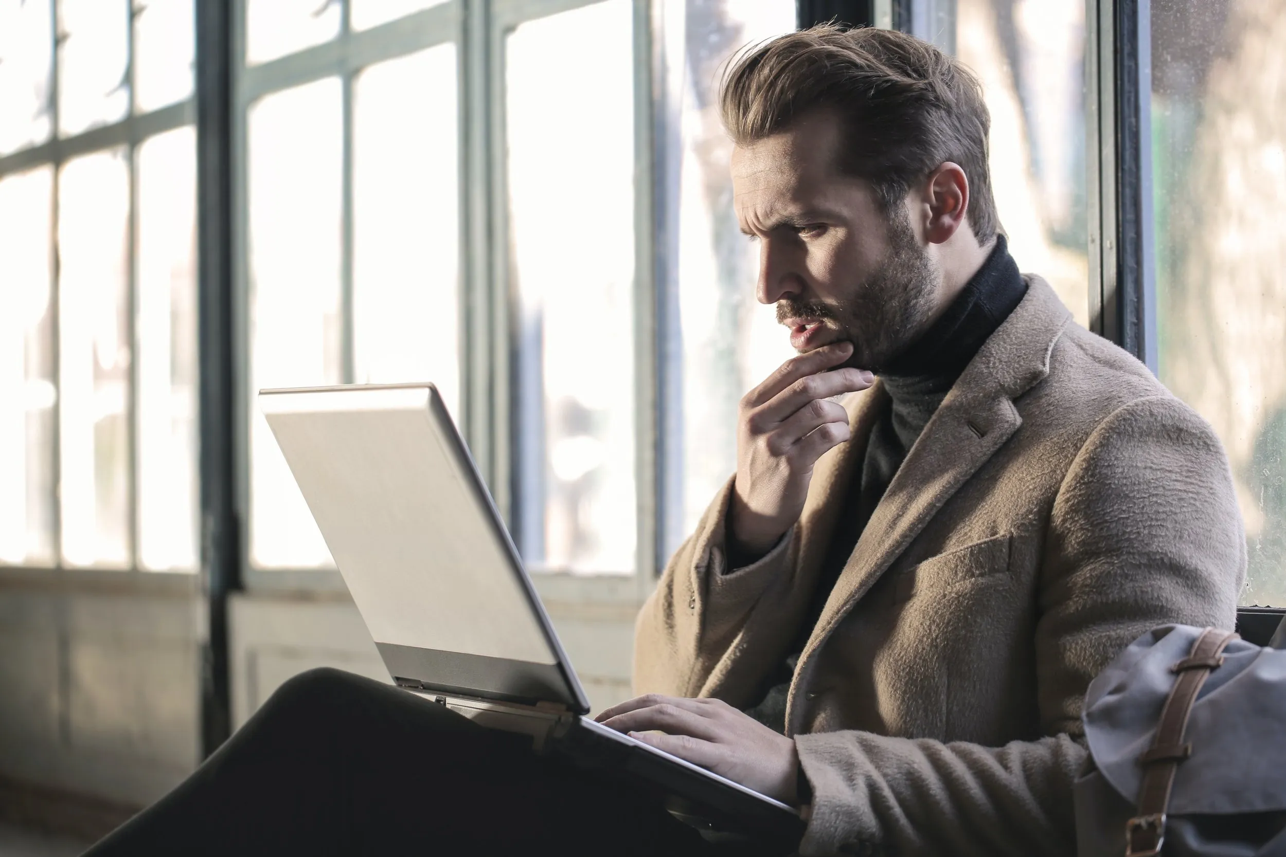 A man deep in thought sitting down with his laptop
