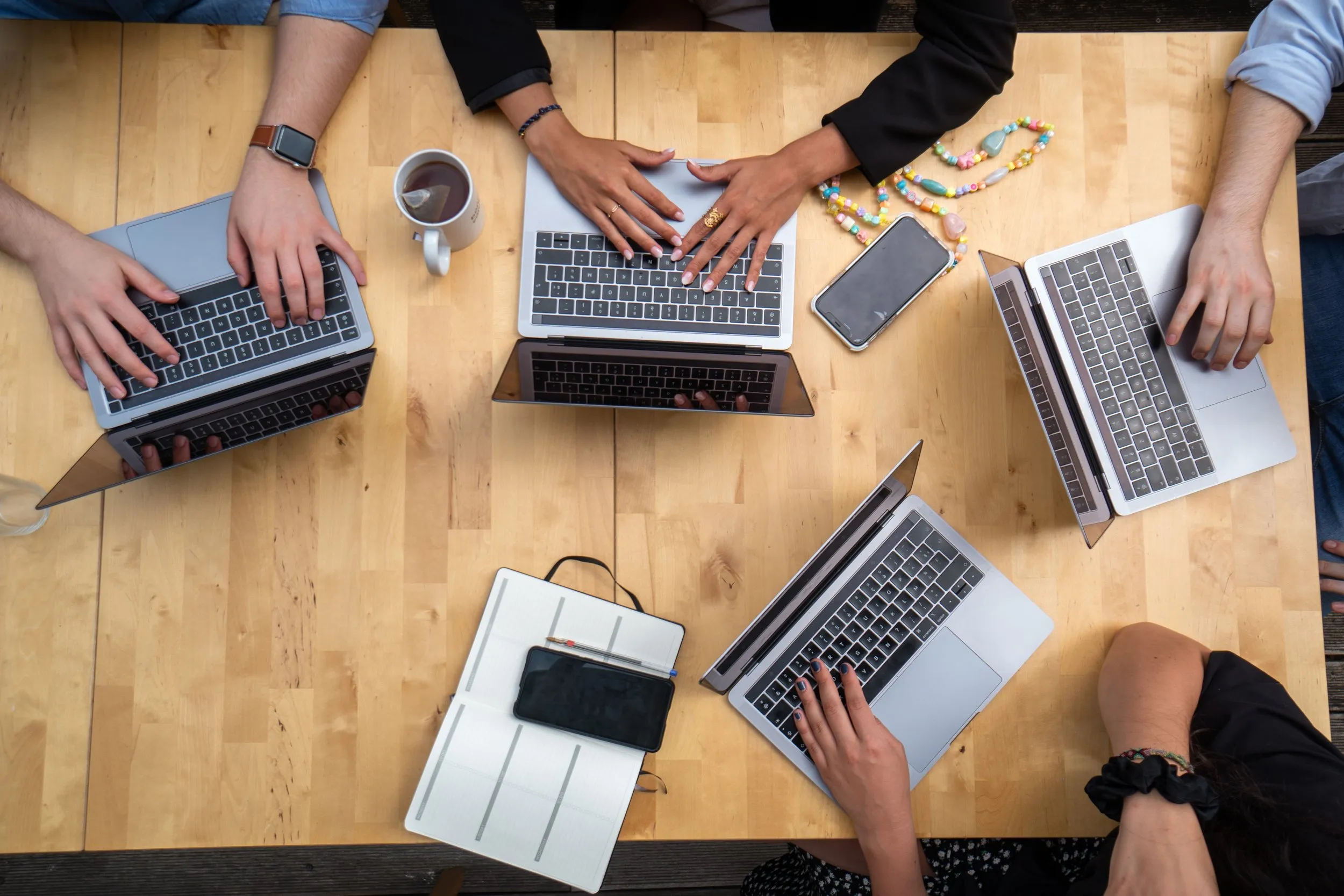 Multiple laptops with hands on a table