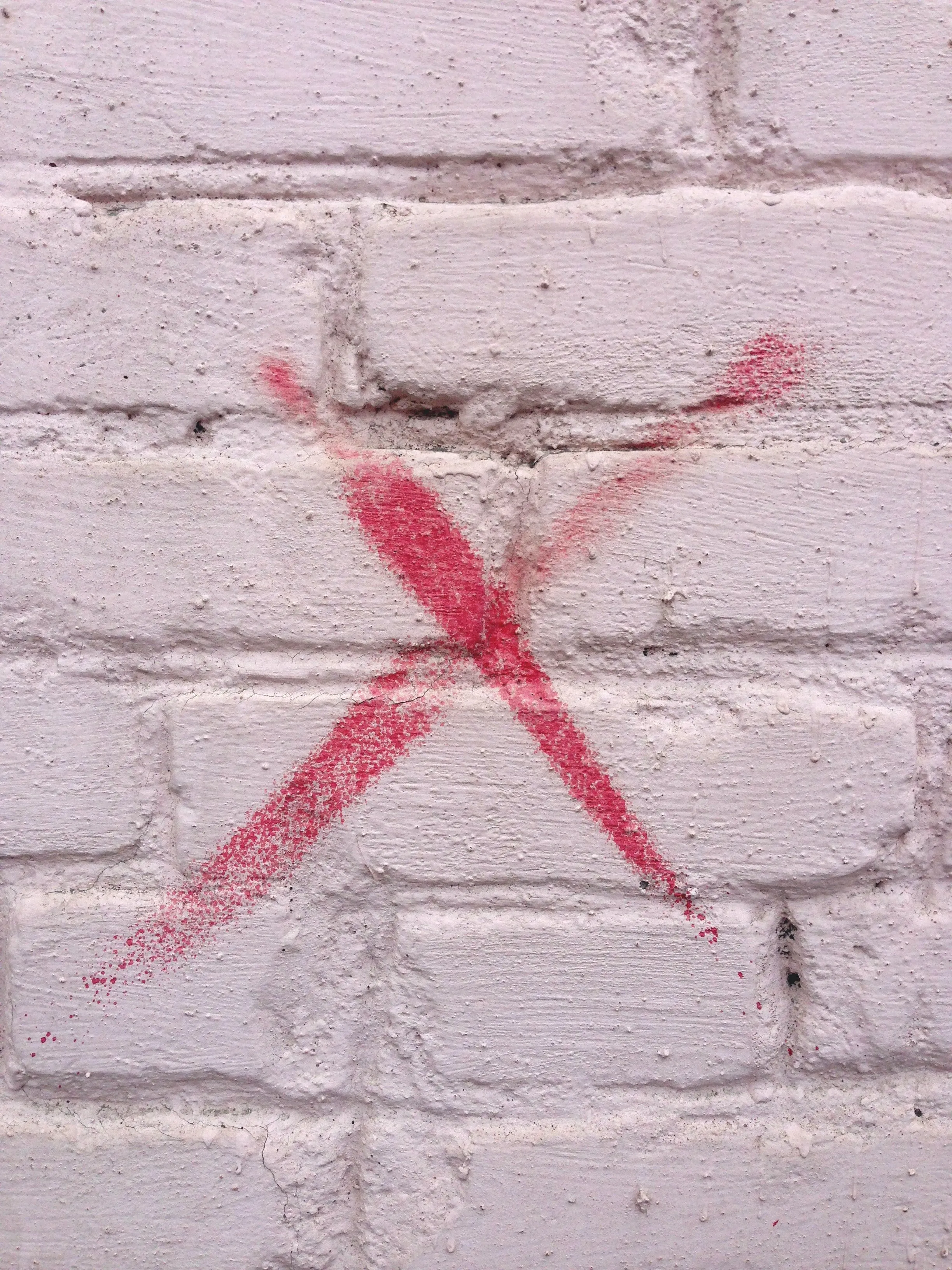 A red "X" on a white brick wall