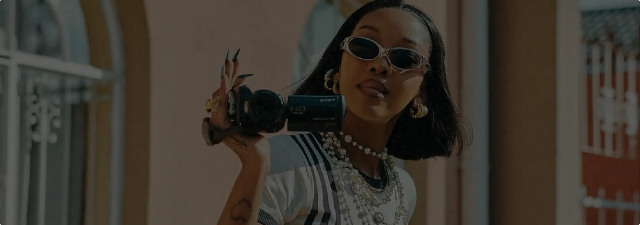 Woman wearing sunglasses and pearl necklaces records video with a handheld Sony camcorder outdoors