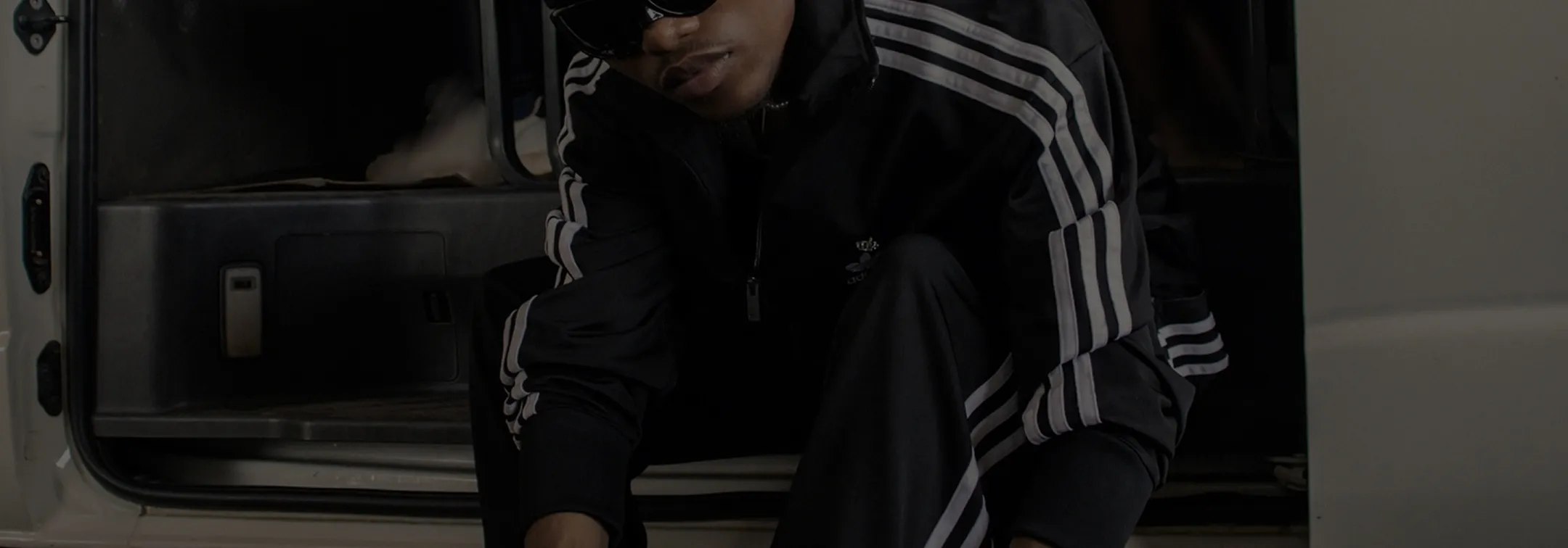 Person in black Adidas tracksuit sitting at the open side door of a white van